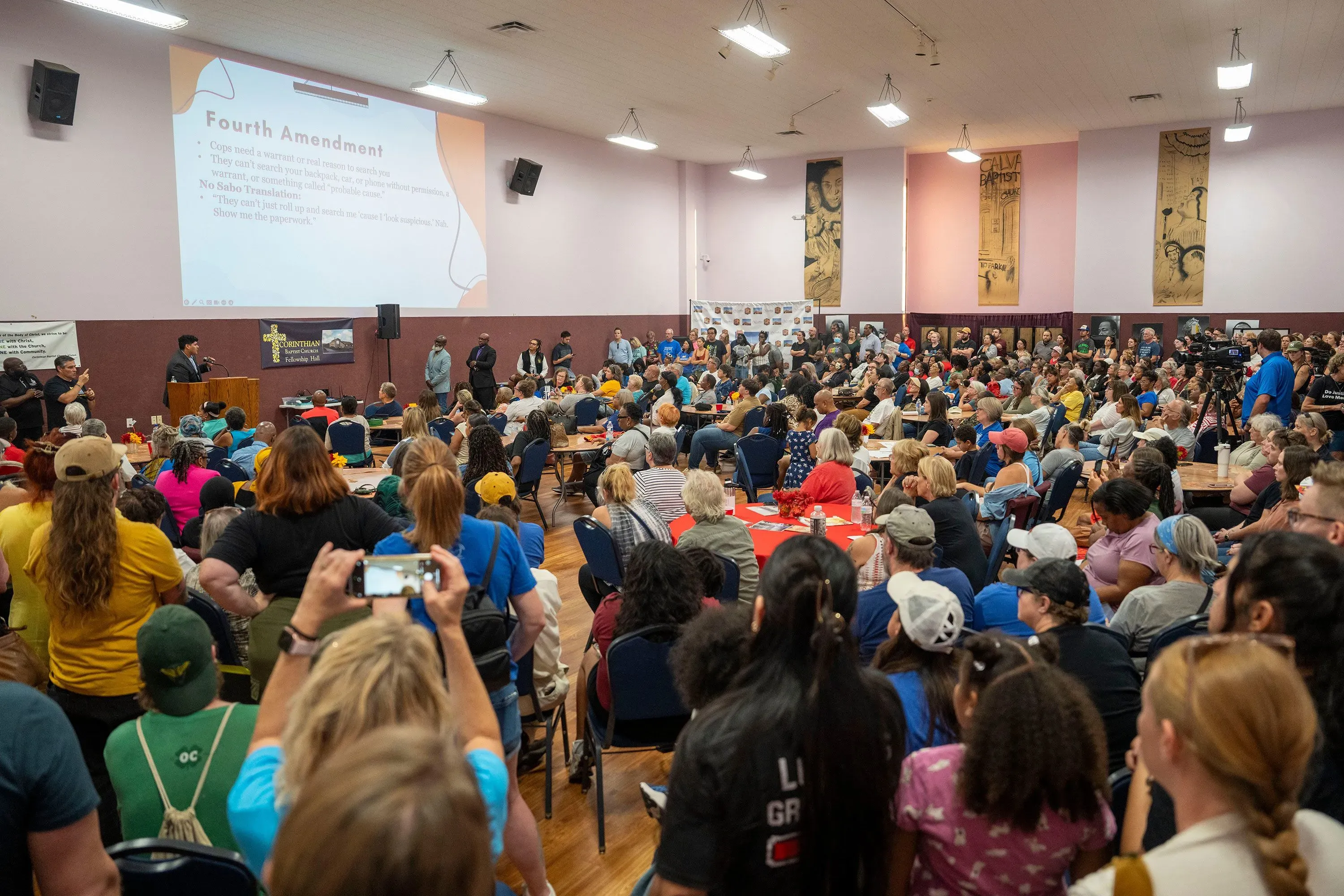 اجتماع حاشد في قاعة، حيث يجلس المئات من الأشخاص في صفوف، مع عرض تقديمي عن التعديل الرابع على الشاشة خلف المتحدث.