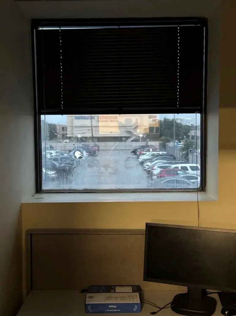 منظر من نافذة مكتب في منشأة إنفاذ قوانين الهجرة والجمارك، يظهر زجاجًا مكسورًا وموقف سيارات بالخارج، بعد إطلاق نار في دالاس.