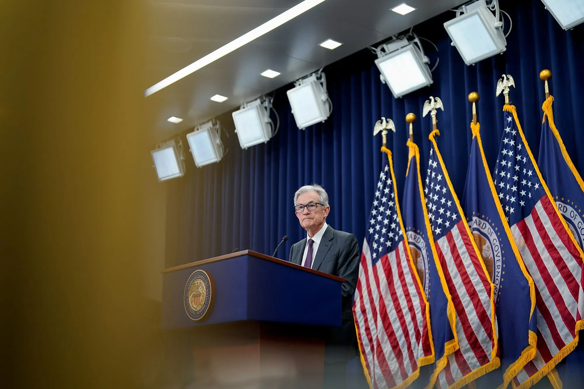 جيروم باول، رئيس مجلس الاحتياطي الفيدرالي، يتحدث في مؤتمر صحفي، مع العلم الأمريكي خلفه، في سياق توقعات خفض أسعار الفائدة.