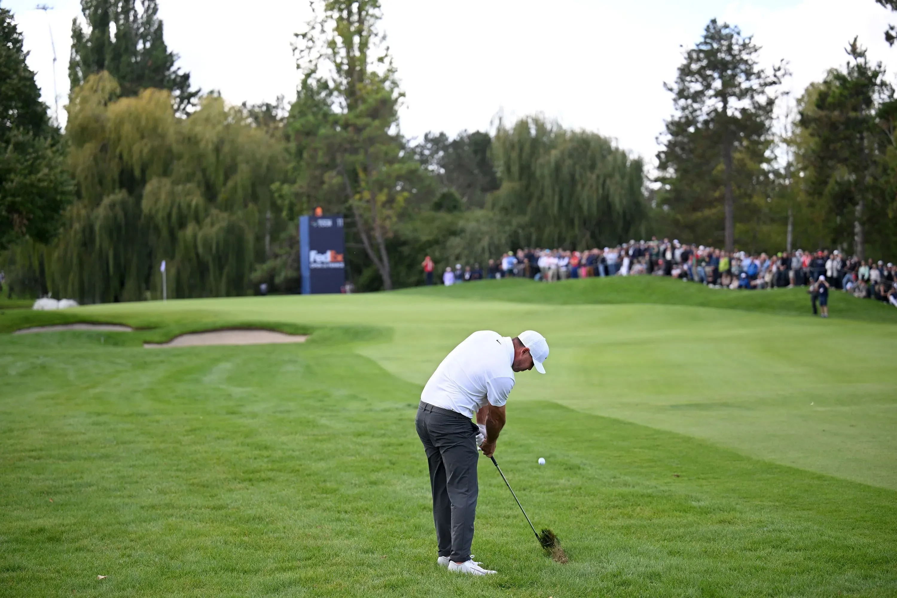 لاعب جولف يقوم بضرب الكرة على ملعب أخضر، مع جمهور كبير في الخلفية، مما يعكس أجواء المنافسة في جولة رابطة محترفي الجولف.