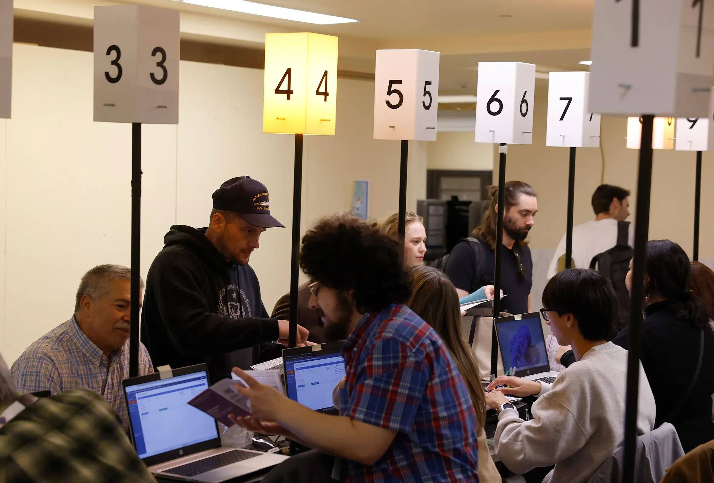 مواطنون يتفاعلون في مركز اقتراع بولاية كاليفورنيا، مع وجود لافتات توضح أرقام الاقتراع، في سياق الانتخابات التمهيدية.