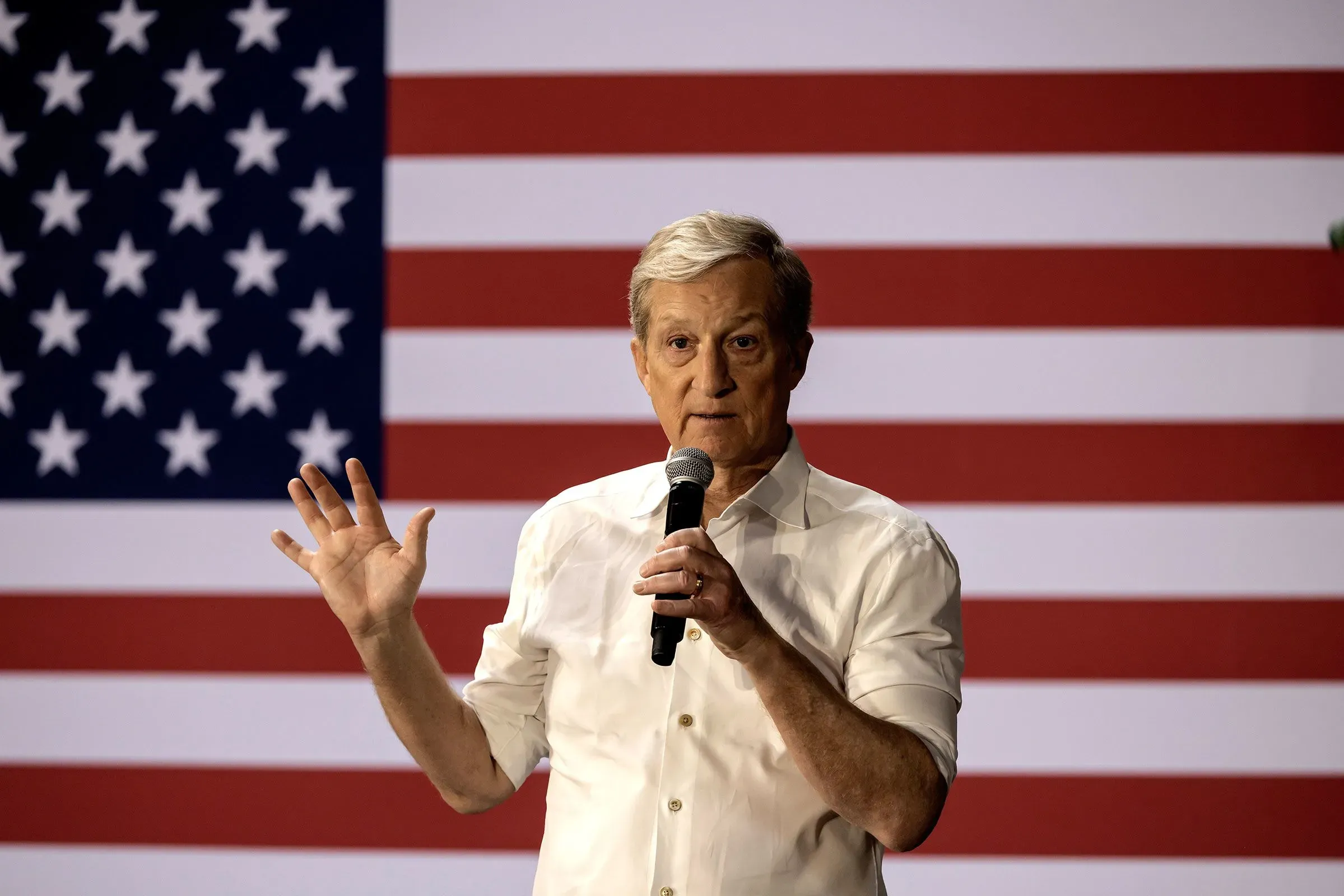 توم ستاير يتحدث في حدث سياسي أمام علم الولايات المتحدة، معبرًا عن آرائه حول الانتخابات التمهيدية في كاليفورنيا.