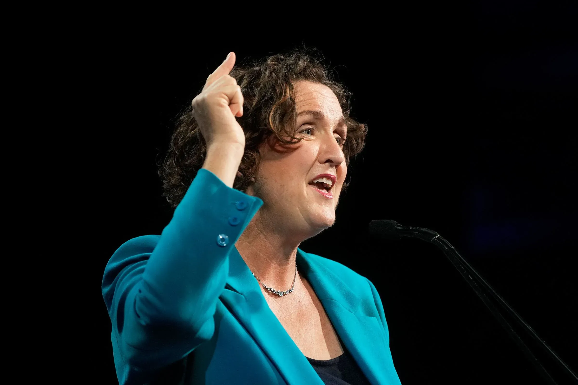 امرأة تتحدث بحماس على المنصة، ترتدي سترة زرقاء، تعبر عن آرائها حول الانتخابات التمهيدية في كاليفورنيا.