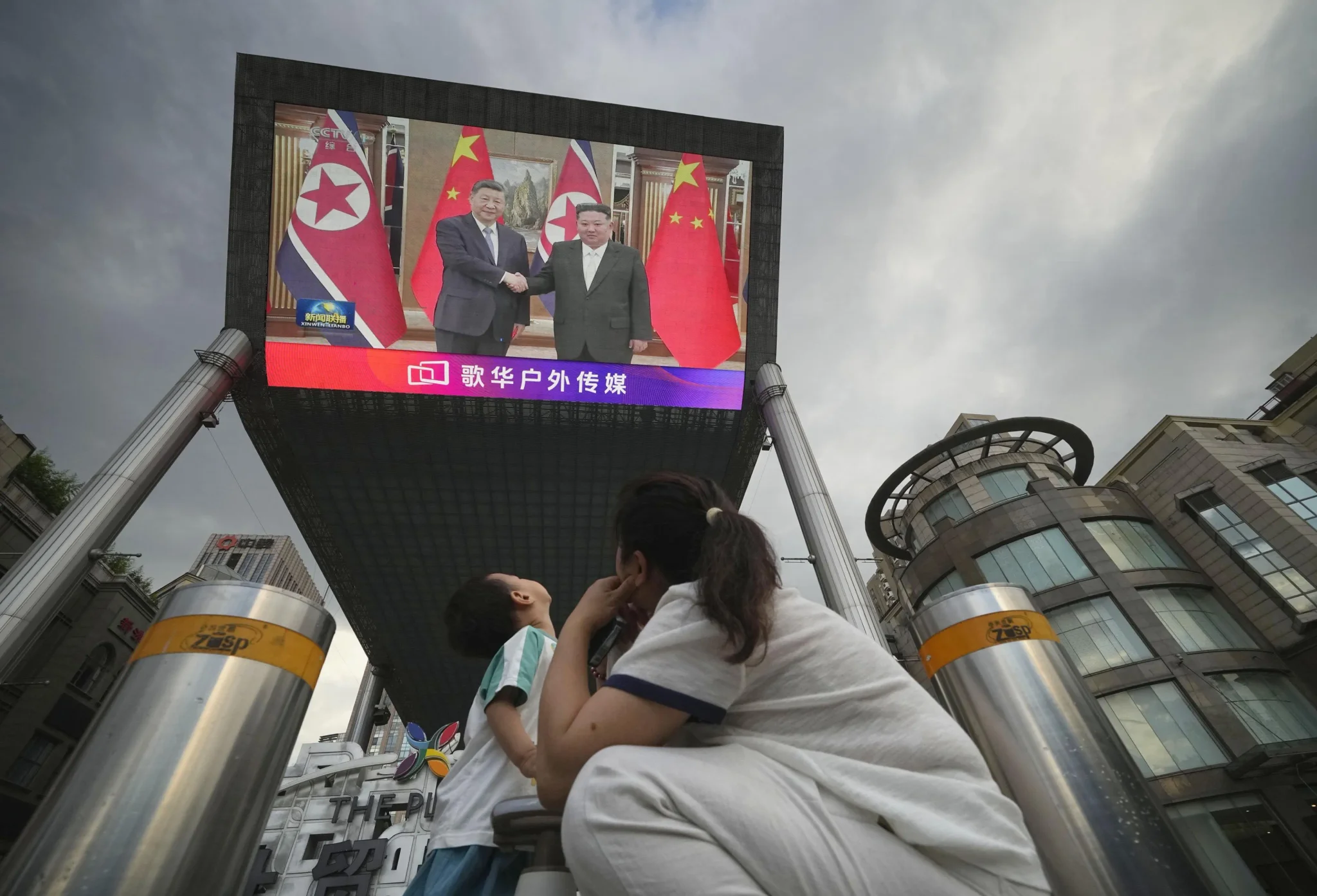 شاشة عملاقة تعرض لقاء Xi Jinping وKim Jong Un في بيونغ يانغ، مع العلمين الصيني والكوري الشمالي، بينما يتابع المشاهدون من الأسفل.