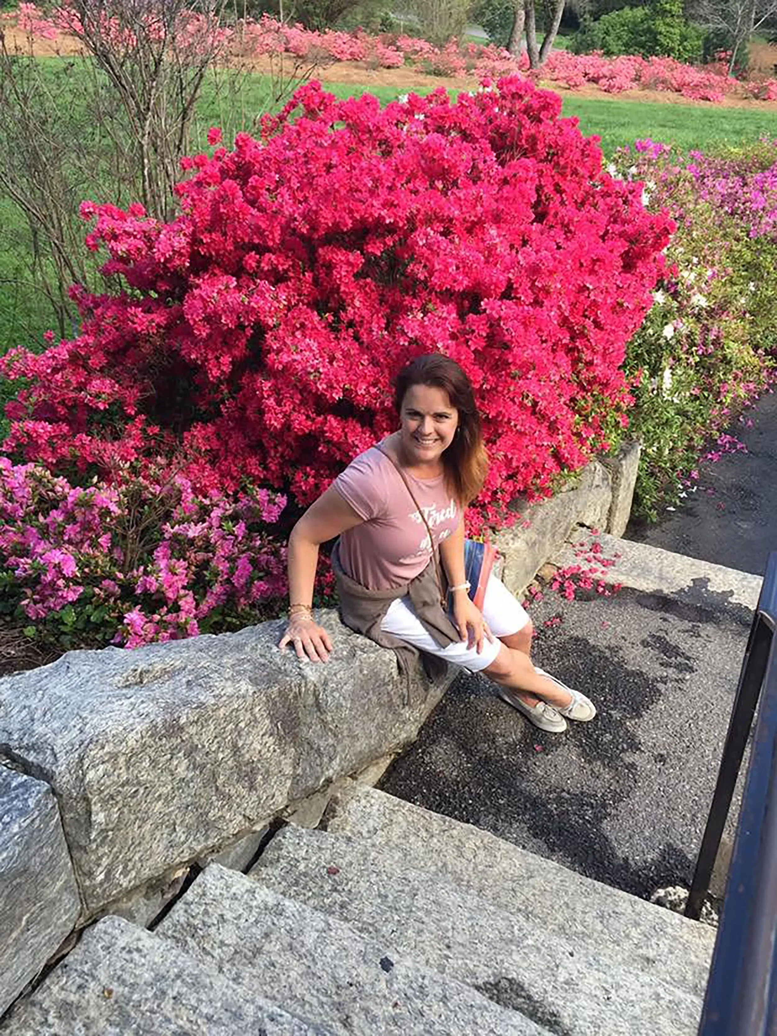 أنجيلا كريغ جالسة على صخرة بجانب أزهار زهرية، تعكس حالتها الصحية المتدهورة وأثرها العاطفي في ظل عدم وجود تشخيص واضح.