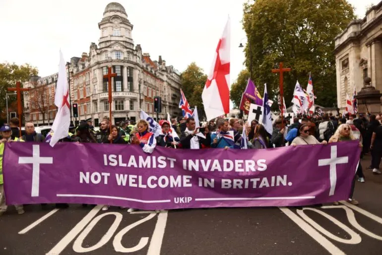 مظاهرة في لندن تضم مجموعة من الأشخاص يحملون لافتة تتضمن رسالة معادية للمهاجرين، في سياق النقاش حول سياسات الهجرة البريطانية.