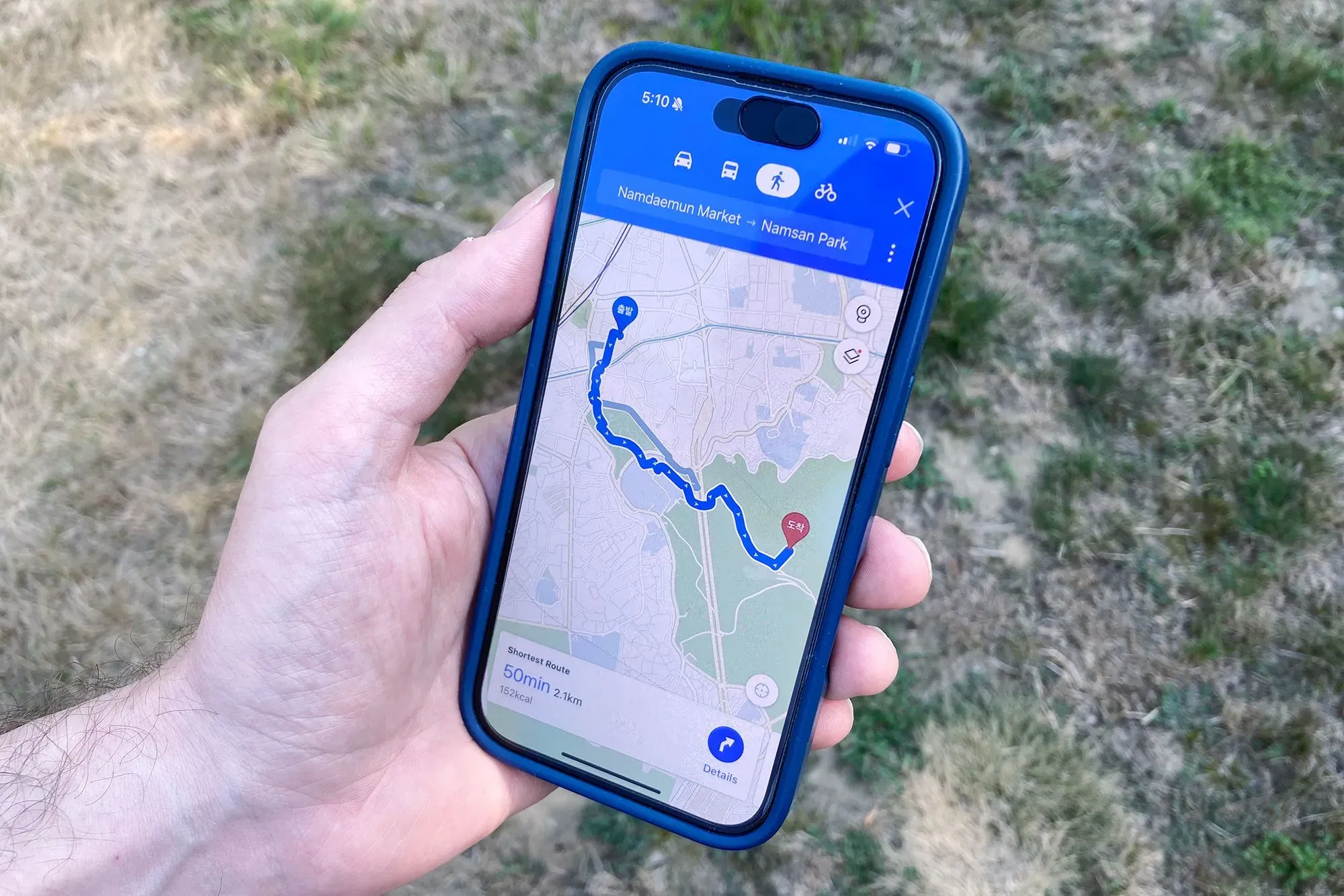 تظهر الصورة شخصًا يحمل هاتفًا ذكيًا يعرض خريطة على تطبيق خرائط جوجل، مع توجيهات من سوق نامدايمون إلى حديقة نامسان في كوريا الجنوبية.