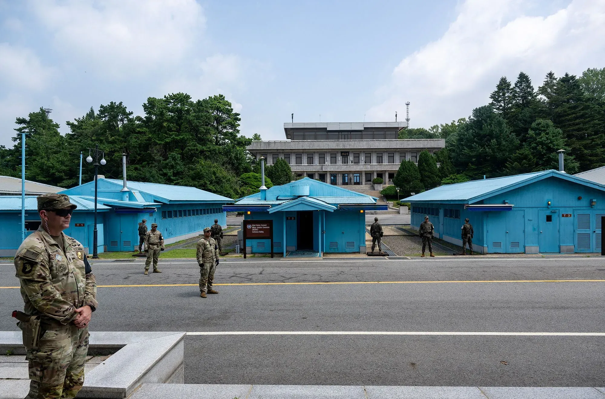 جنود أمريكيون يقفون حراسة أمام مباني زرقاء في المنطقة المنزوعة السلاح بين الكوريتين، مع خلفية طبيعية وأجواء مشمسة.