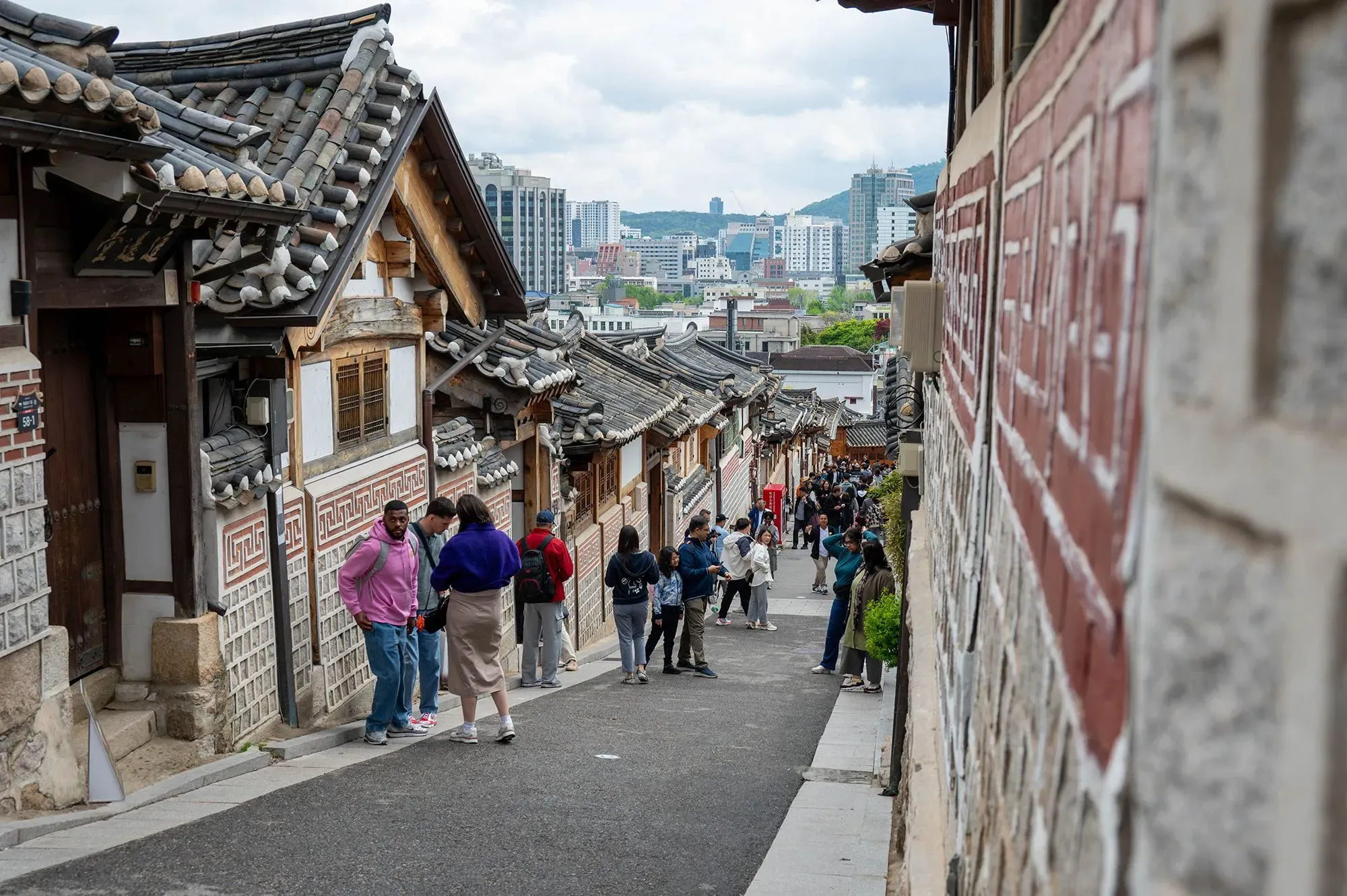 منطقة تاريخية في كوريا الجنوبية، تظهر فيها منازل تقليدية مع زوار يتجولون في الشارع. تعكس الصورة تباين العمارة القديمة والحديثة.