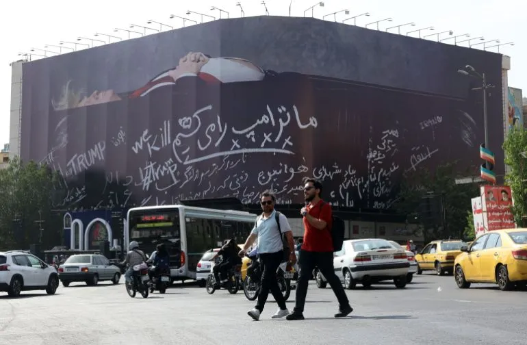 جدارية ضخمة في طهران تحمل شعارات معارضة للرئيس الأمريكي ترامب وسط حركة مرور نشطة في المدينة، تعكس التوترات بين إيران والولايات المتحدة.