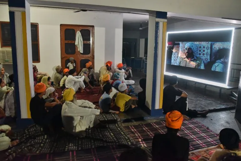 مجموعة من السيخ يرتدون العمائم البرتقالية يشاهدون عرضاً لفيلم Satluj في تجمع داخلي بالبنجاب، الهند، يعكس التوتر حول قضايا الانفصال وحقوق الإنسان.