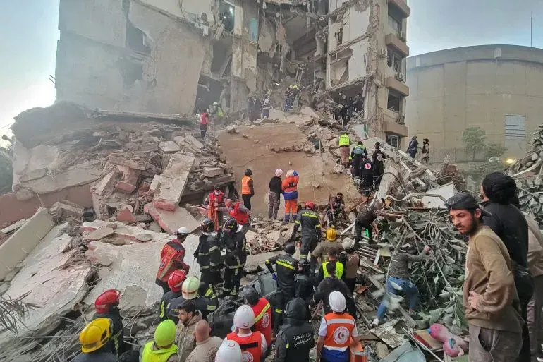 فرق الإنقاذ تعمل في موقع انهيار مبنى في لبنان، حيث تضررت المنطقة بشدة جراء الهجمات الجوية، مع وجود العديد من الضحايا والمصابين.