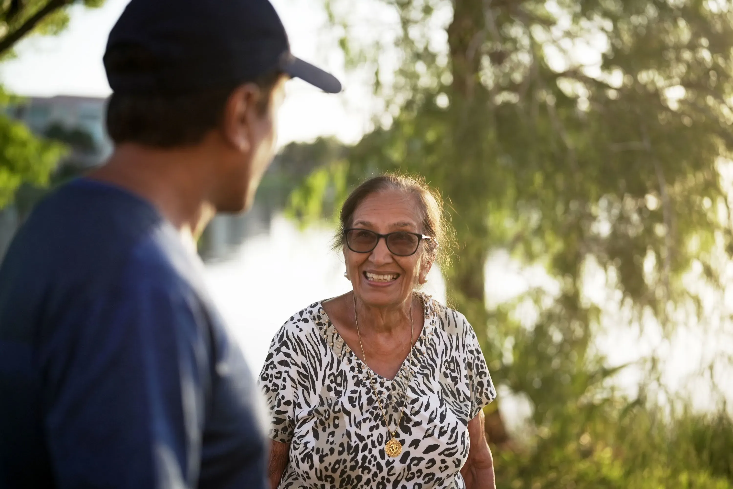 رجل وامرأة مسنّة يبتسمان ويتحدثان في بيئة خارجية، مما يعكس أهمية الدعم الاجتماعي في تخفيف الألم.