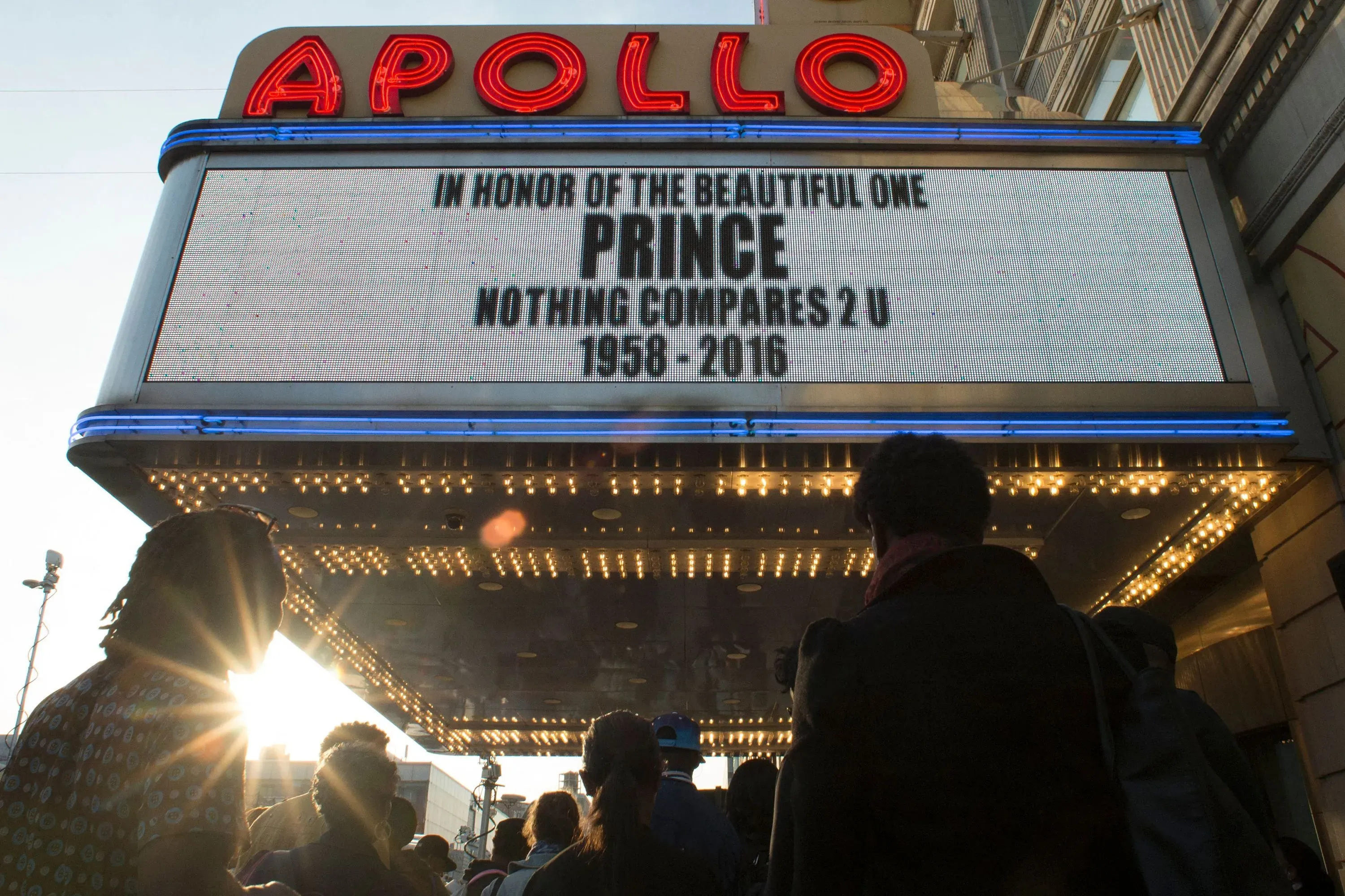 شاشة عرض في مسرح أبولو تكرم الفنان برنس، مع عبارة "لا شيء يقارن بك" وتاريخ ميلاده ووفاته، بينما يتجمع الناس أمام المسرح.