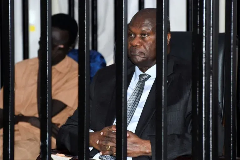 رياك مشار، النائب الأول لرئيس جنوب السودان، يجلس داخل قاعة محكمة محاطة بالأسلاك، مع تهم تتعلق بالإرهاب والخيانة.