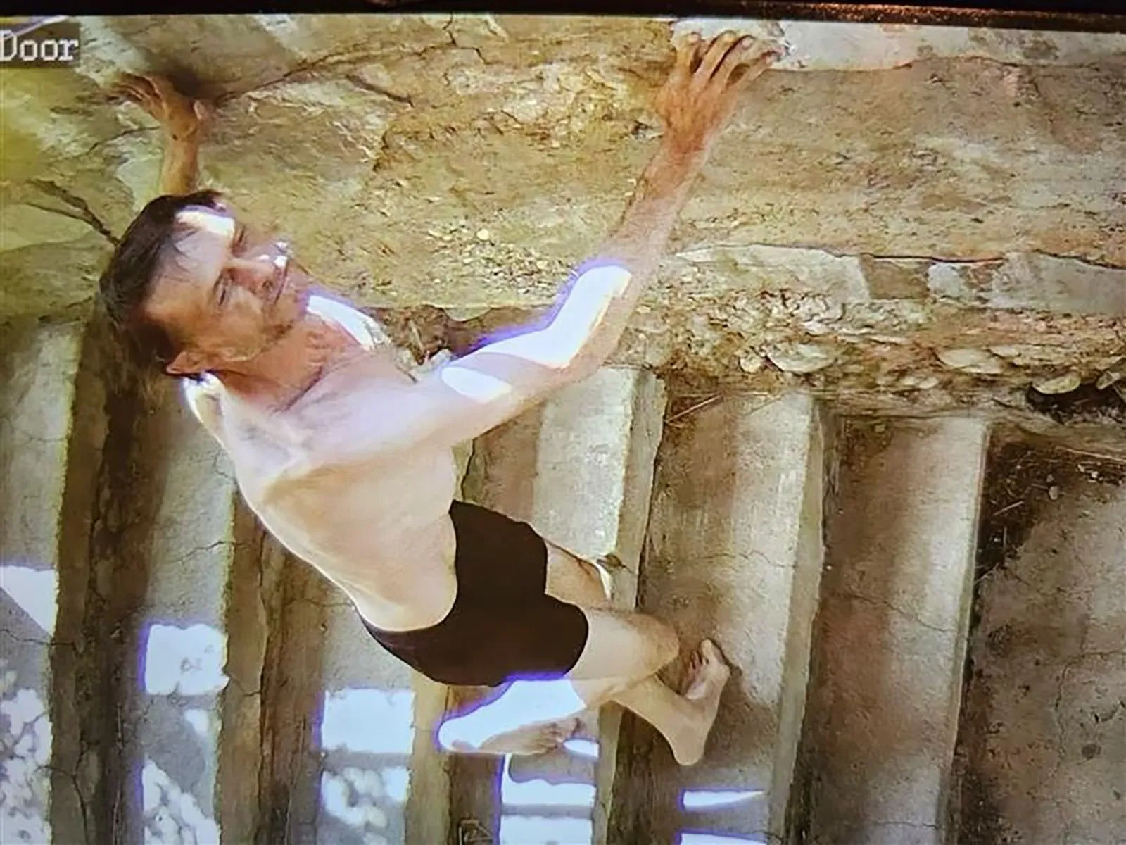 رجل يتسلق جدارًا في منطقة وعرة، يظهر في ملابس داخلية، مما يعكس حالة هروب مشبوه من السلطات بعد حادثة إطلاق نار في مونتانا.