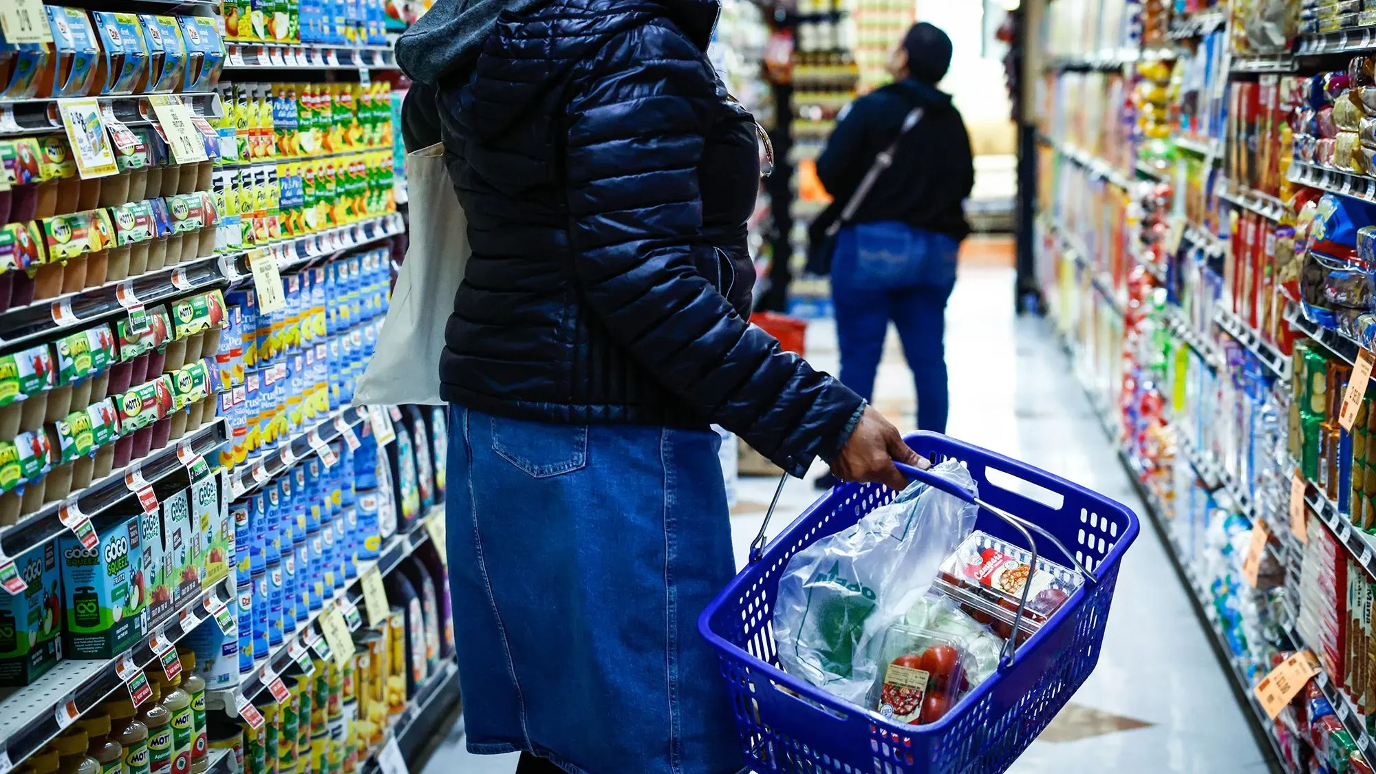 امرأة تحمل سلة تسوق مليئة بالمواد الغذائية في ممر سوبر ماركت، تعكس تحديات تكاليف المعيشة والاقتصاد الأمريكي الحالي.