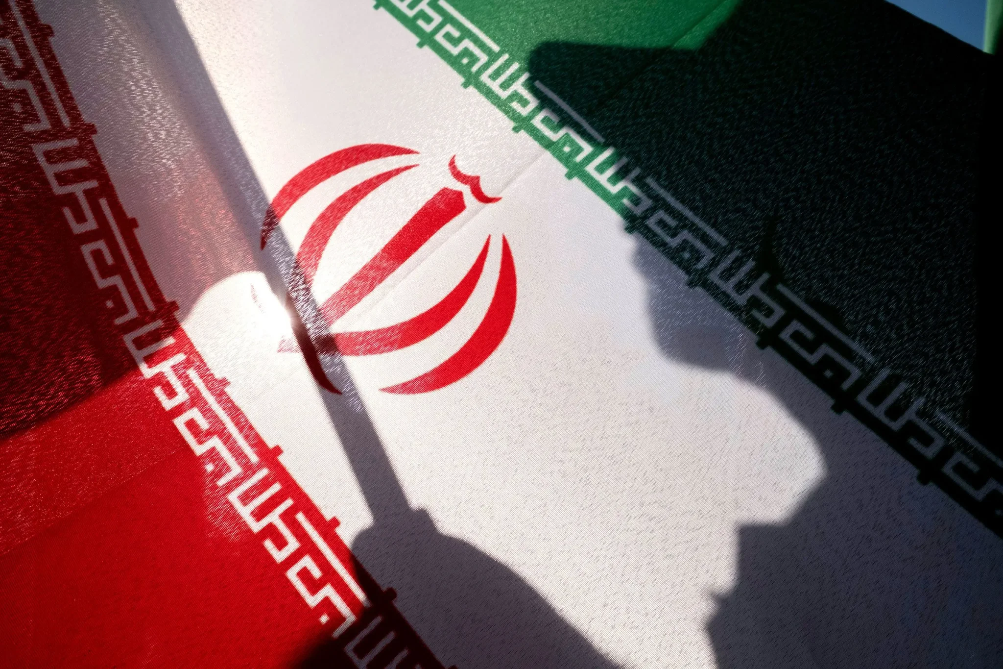 ظل ظل شخص يحمل العلم الإيراني على خلفية العلم، مع التركيز على تأثير الحرب في إيران على الاقتصاد وأسعار الوقود.