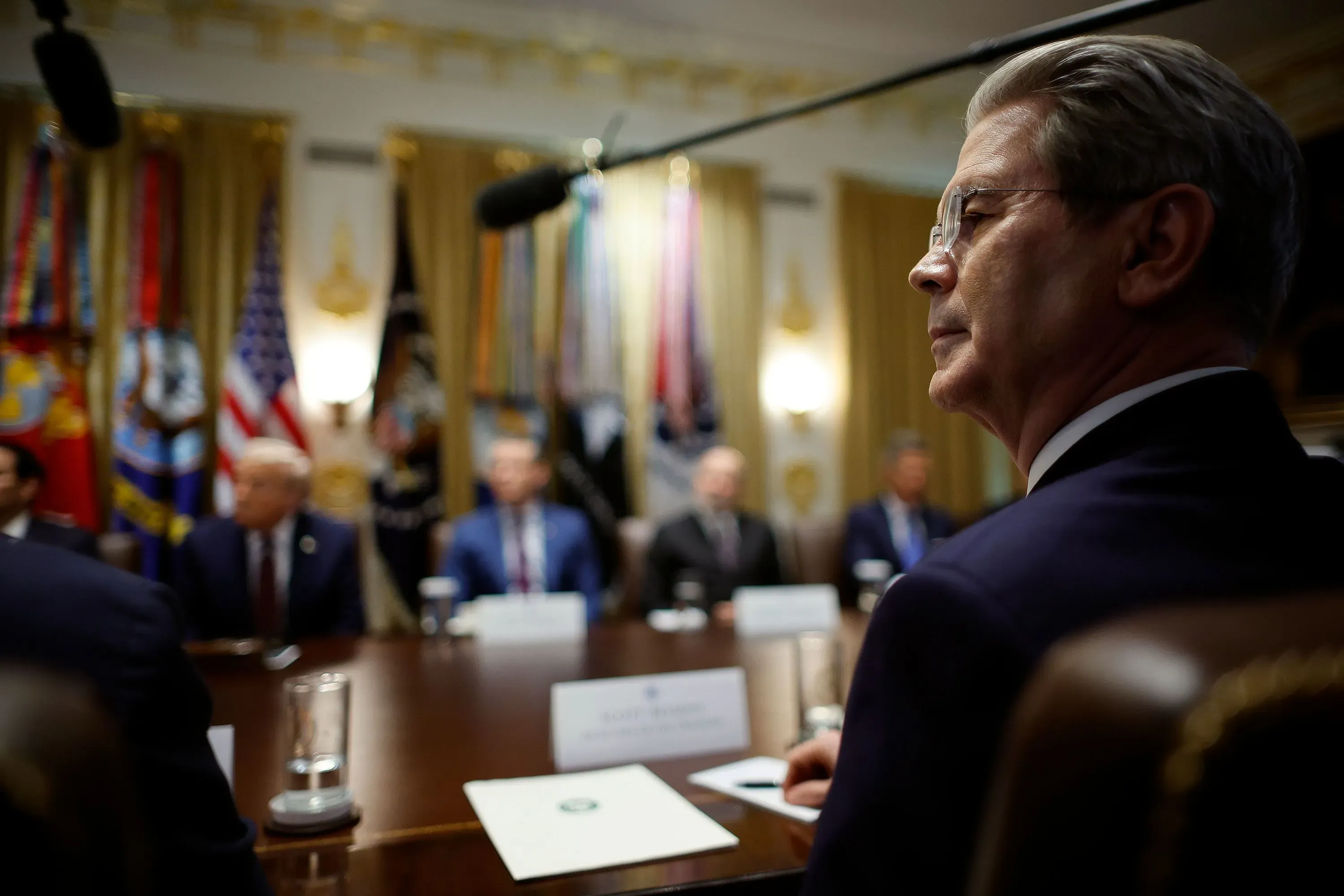 اجتماع في البيت الأبيض يظهر مسؤولين حكوميين، مع التركيز على أحدهم الذي يبدو قلقًا، وسط أعلام الولايات المتحدة.