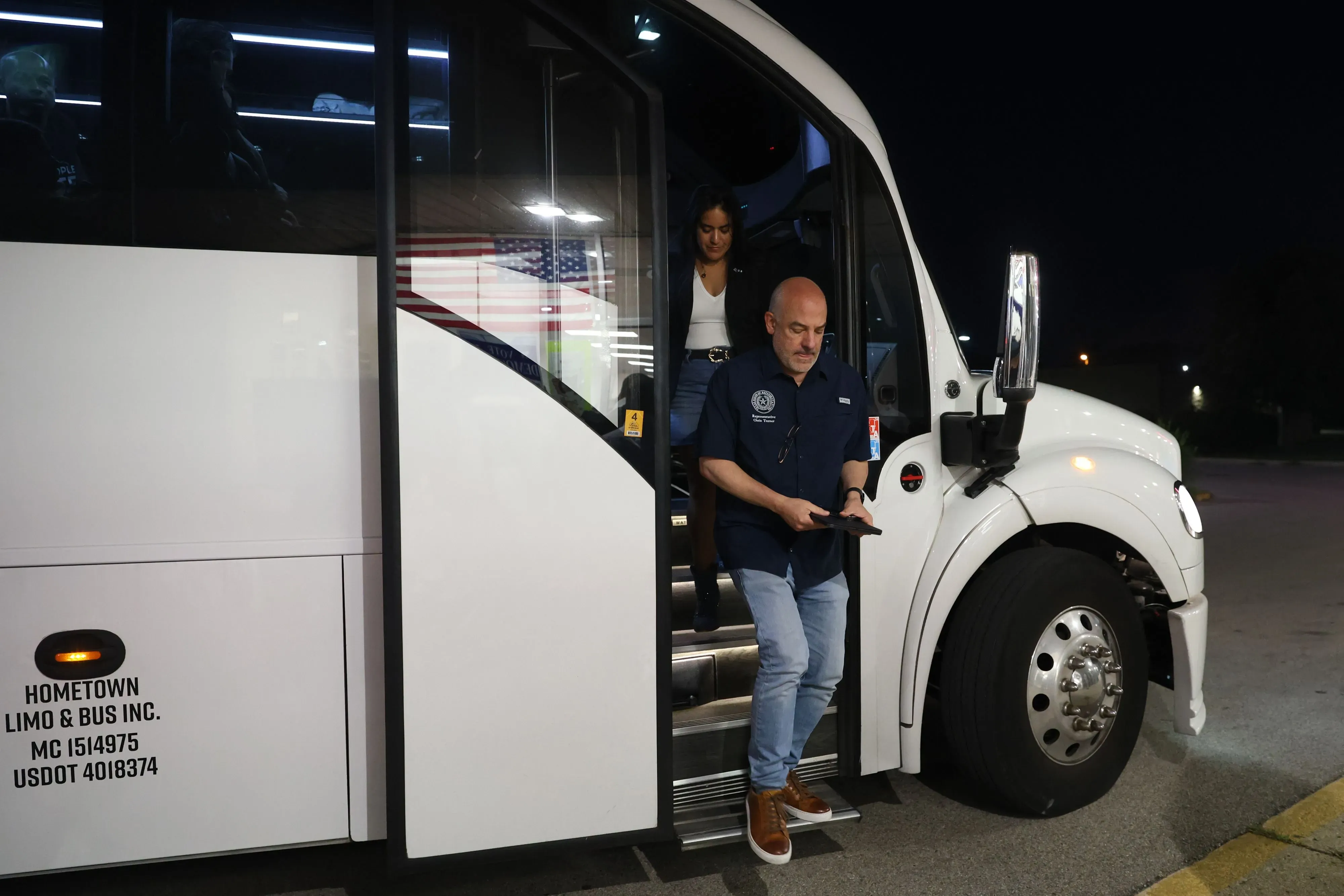 مشرعون ديمقراطيون يغادرون حافلة في الليل، مع العلم الأمريكي في الخلفية، في سياق جهودهم لمواجهة إعادة تقسيم الدوائر الانتخابية في تكساس.