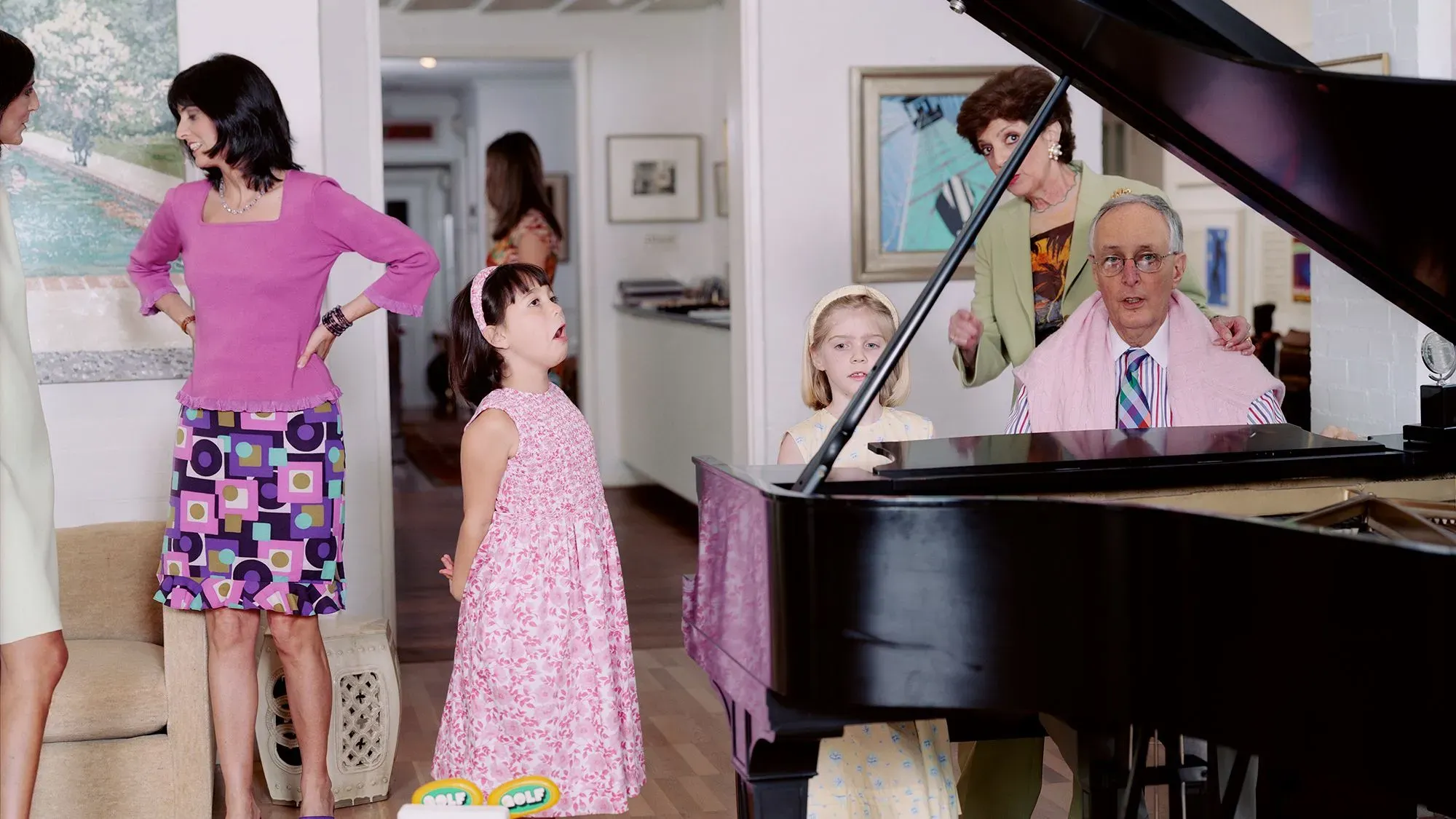 مجموعة من الأشخاص في غرفة معيشة، حيث تعزف امرأة على البيانو بينما يستمع الآخرون، مما يعكس اللحظات العائلية الحميمية.