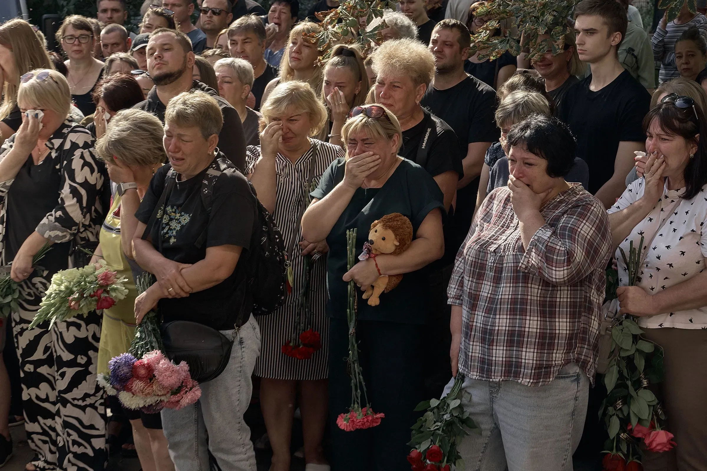 مجموعة من الأشخاص في حالة حزن، بعضهم يحملون زهورًا، أثناء مراسم تأبين في أوكرانيا، تعبيرًا عن دعمهم في ظل الظروف الصعبة.