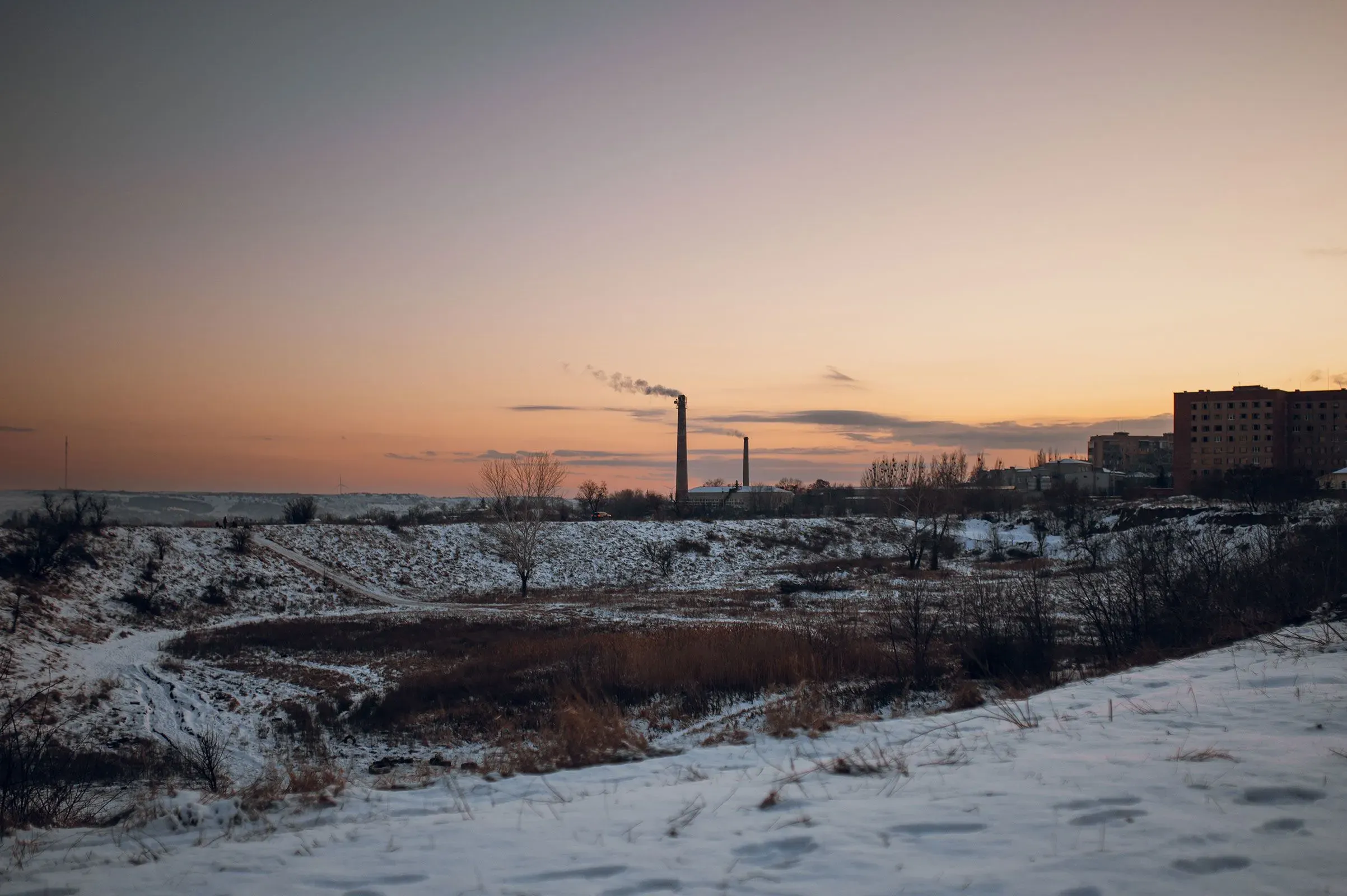 منظر طبيعي شتوي في أوكرانيا يظهر دخانًا يتصاعد من مداخن المصانع تحت سماء غائمة، مع وجود الثلوج على الأرض.
