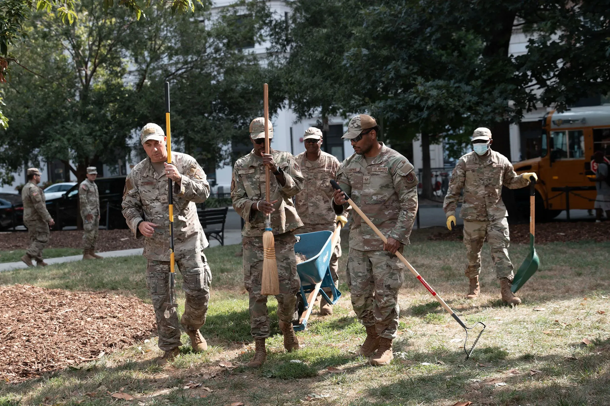 جنود من الحرس الوطني يعملون في مشروع تجميل في العاصمة واشنطن، يحملون أدوات مثل المجارف والمكانس، أثناء تأدية مهامهم.