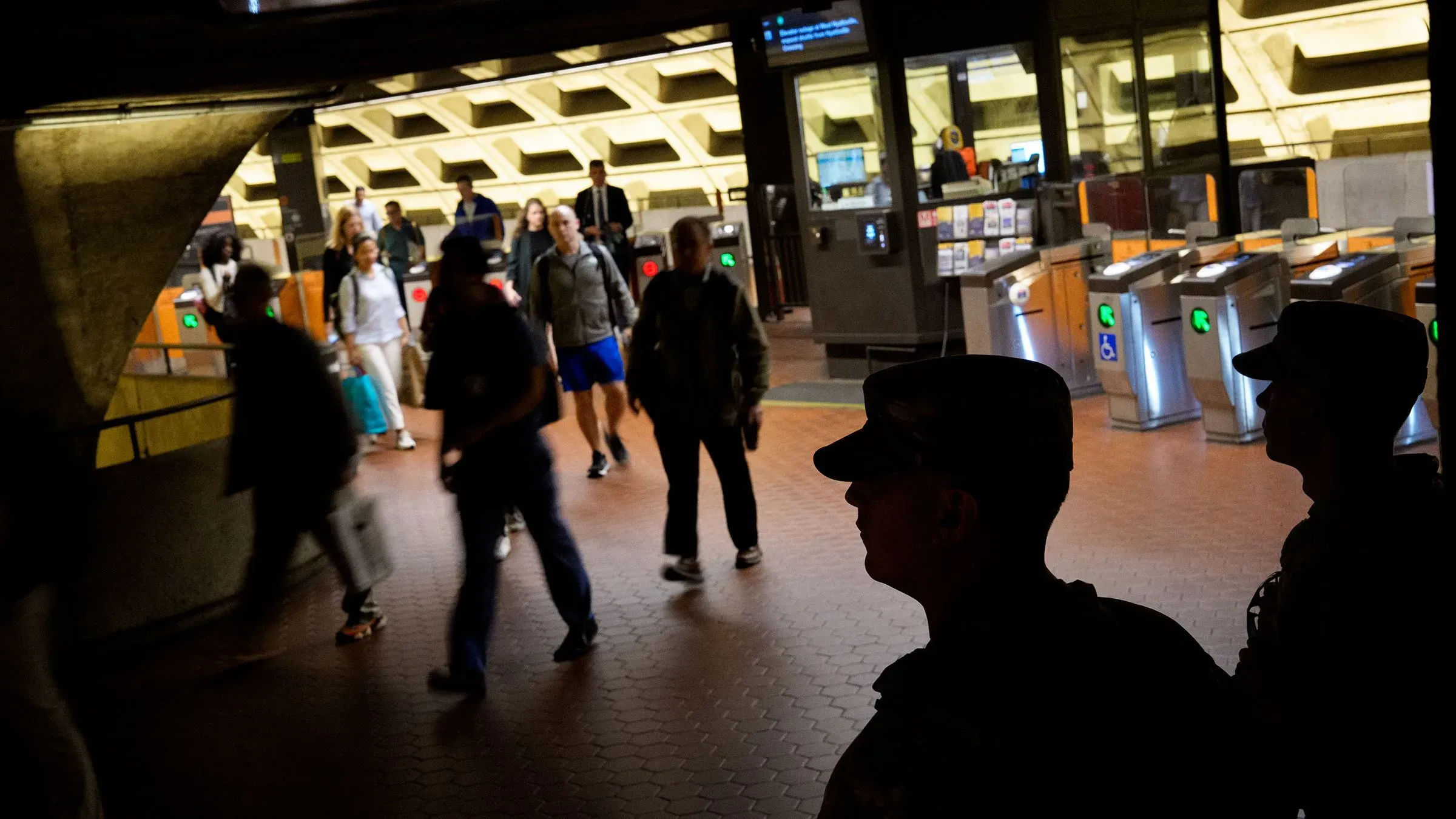 جنود من الحرس الوطني يقومون بدورية في محطة مترو، مع وجود مسافرين يتنقلون في الخلفية، مما يعكس الأجواء الأمنية في العاصمة.