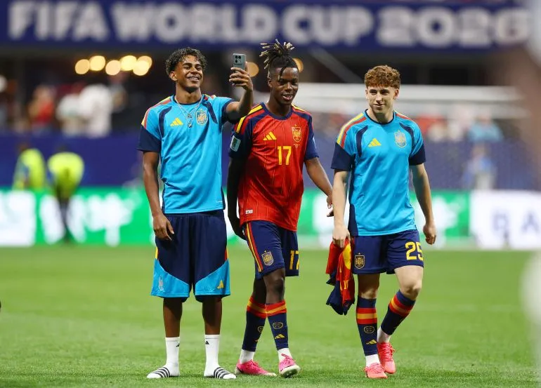 ثلاثة لاعبين من منتخب إسبانيا يحتفلون بعد مباراة، أحدهم يلتقط سيلفي، مع خلفية تشير إلى كأس العالم 2026.
