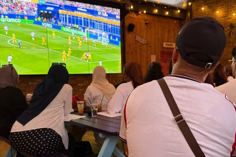 مشجعون مسلمون يشاهدون مباراة إنجلترا في كأس العالم داخل مقهى بلندن، يعكسون دعمهم للاعب Djed Spence وتأثير تمثيله التاريخي.