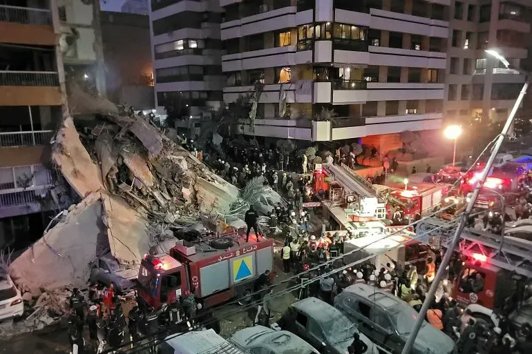 تظهر الصورة انهيار جزء من مبنى في لبنان، مع وجود سيارات إطفاء وفرق إنقاذ تعمل على إنقاذ الضحايا وسط تجمع حشود من الناس.