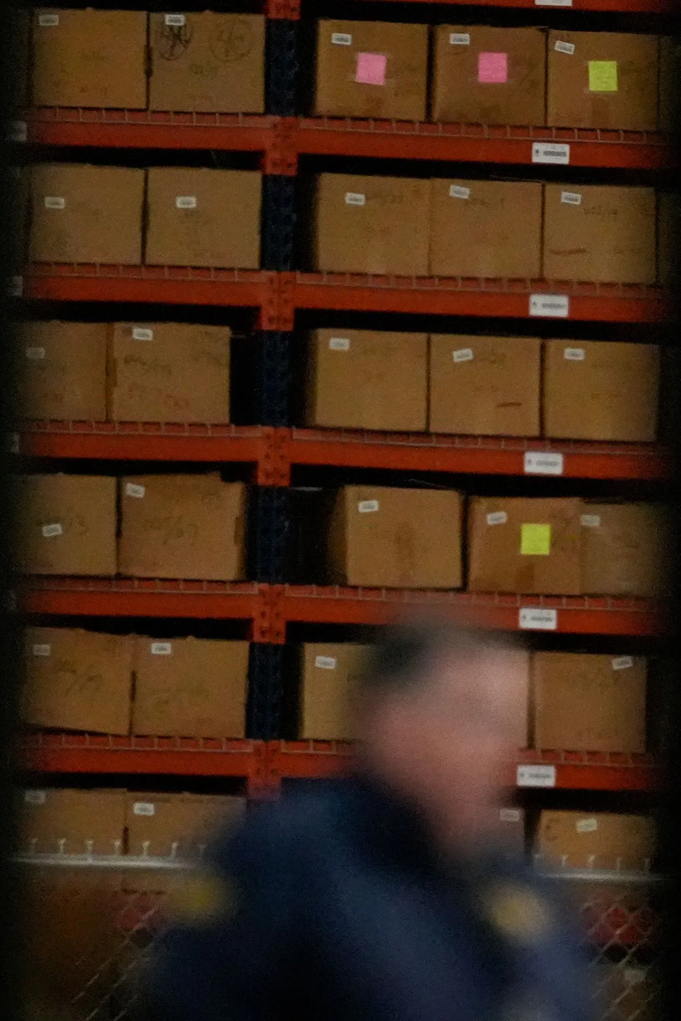 صناديق اقتراع مؤمنة في مستودع، مع وجود شخص غير واضح في المقدمة، تعكس التوترات حول نزاهة الانتخابات والتهديدات الفيدرالية.