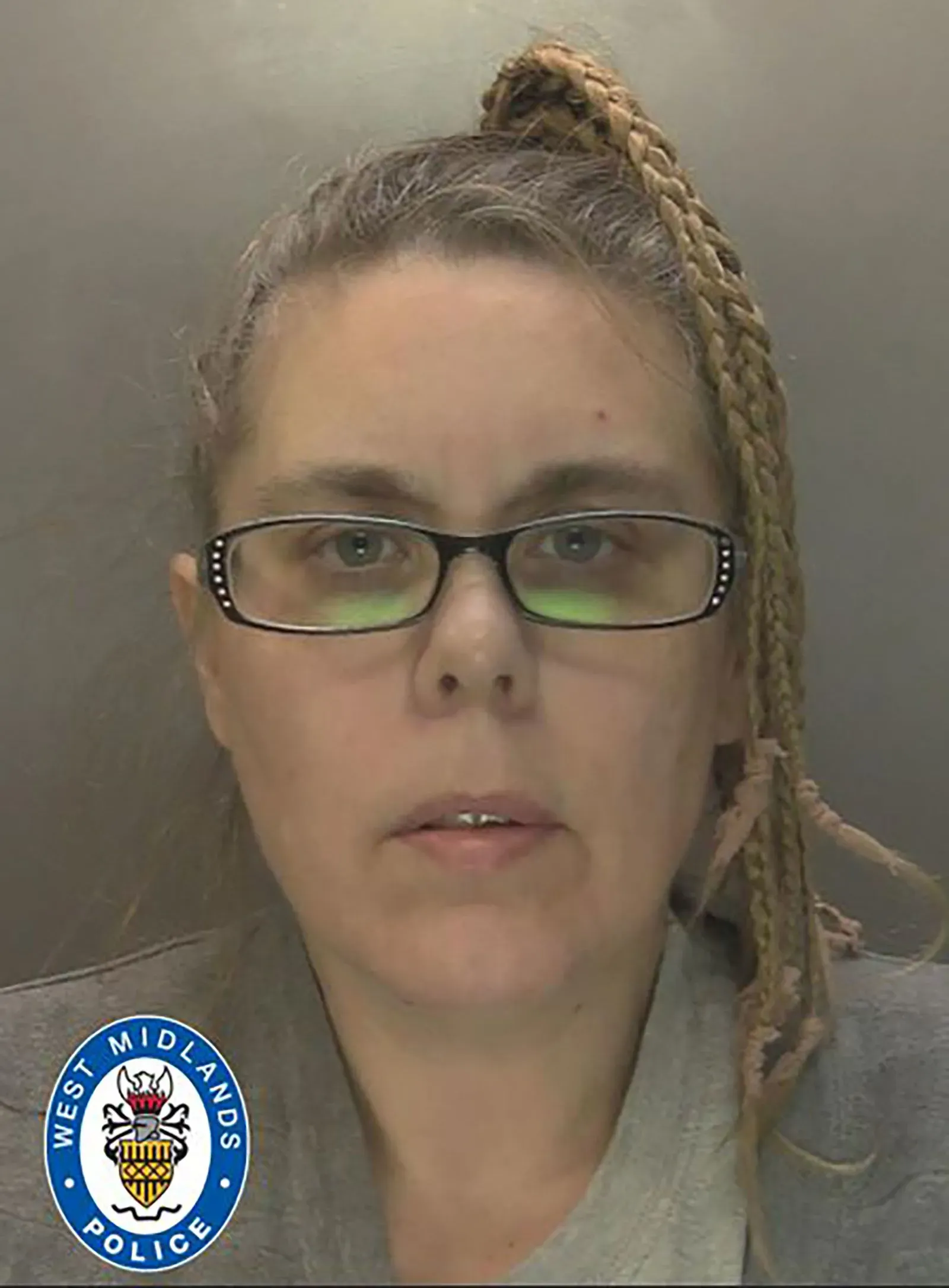 امرأة محجوزة من قبل الشرطة، ترتدي نظارات، وشعرها مضفور، في سياق قضية تآمر على القتل. تعكس الصورة تفاصيل محاكمة معقدة.