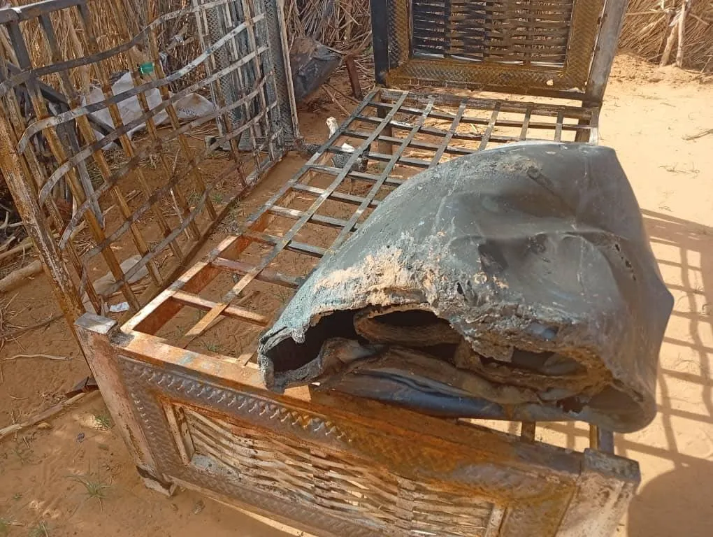 خوذة مدمرة على سرير معدني في الأبيض، تعكس أثر القصف بالطائرات المسيّرة في الحرب الأهلية السودانية وتأثيرها على المدنيين.