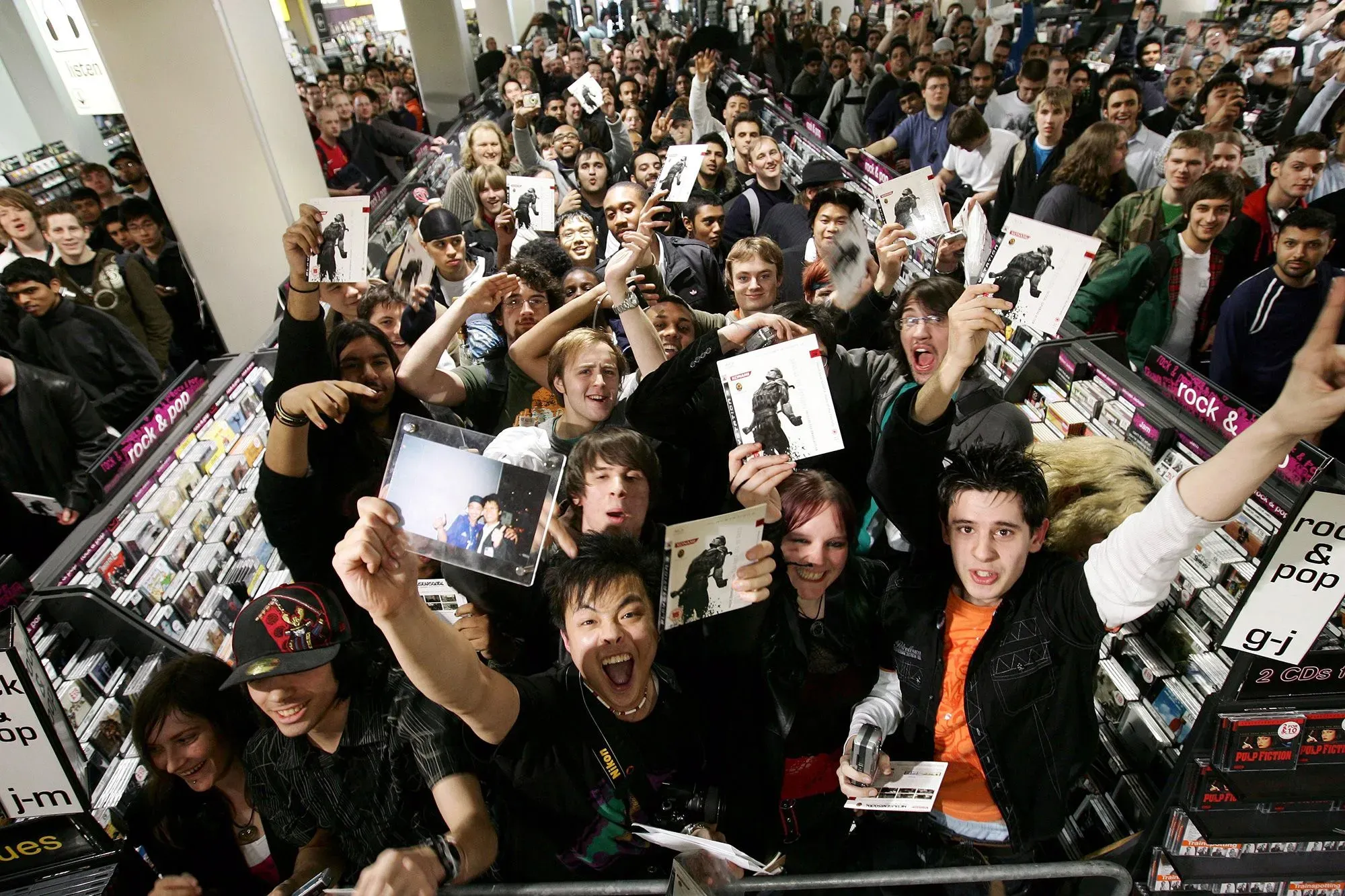 حشد كبير من المعجبين يحتفلون بإطلاق لعبة "ديث ستراندينج 2" في متجر موسيقى، حيث يحملون نسخهم من اللعبة ويعبرون عن حماسهم.