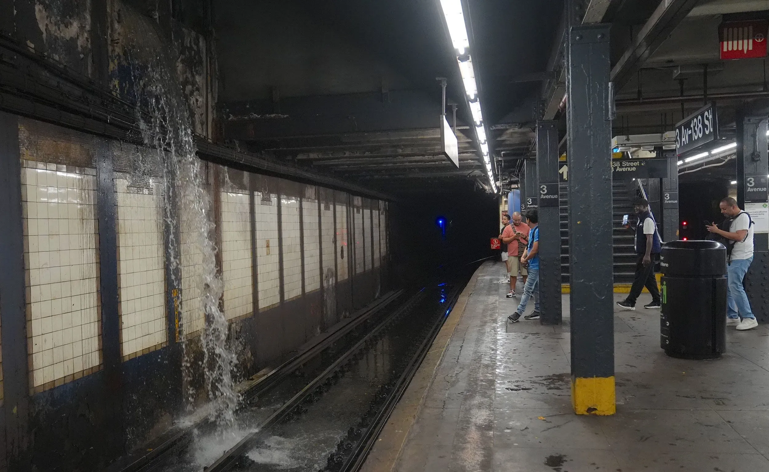 تسرب مياه من سقف محطة مترو أنفاق، حيث يقف الركاب على الرصيف بينما تتجمع المياه على القضبان، مما يعكس تحديات البنية التحتية في مواجهة الطقس القاسي.