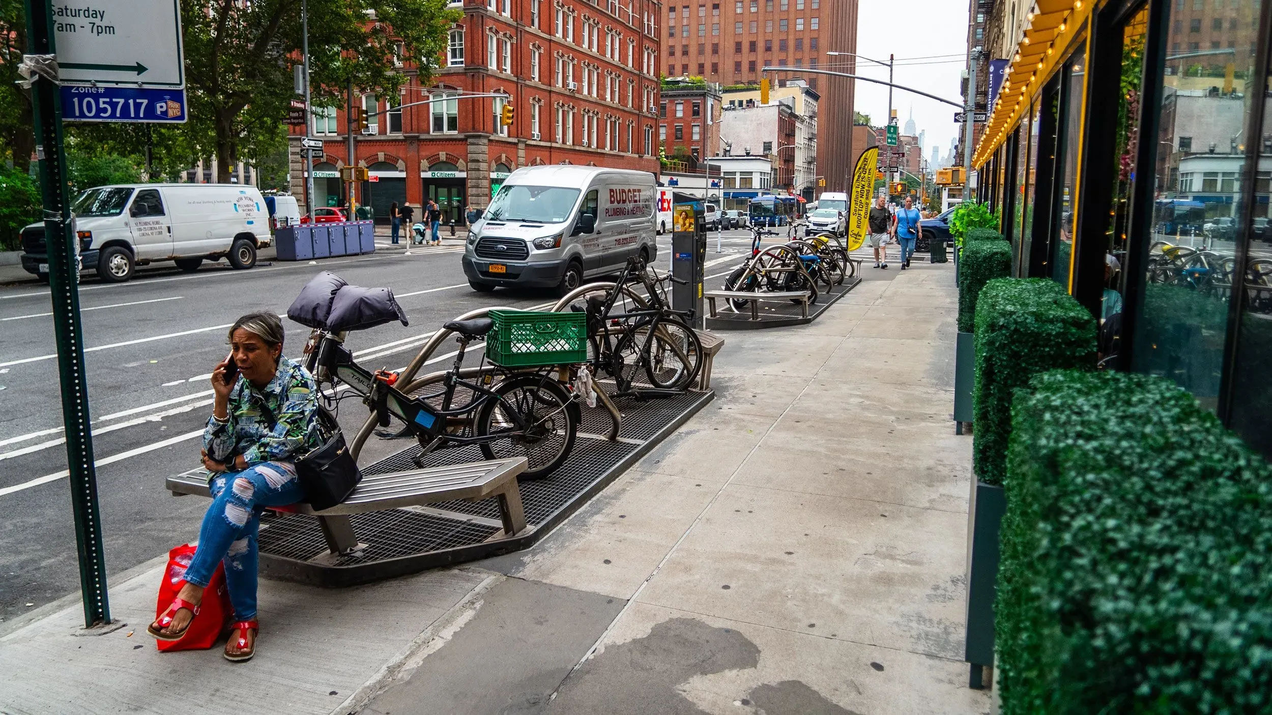 امرأة تتحدث في الهاتف بينما تجلس على مقعد في رصيف بمدينة نيويورك، مع وجود دراجات متوقفة على الجانب.