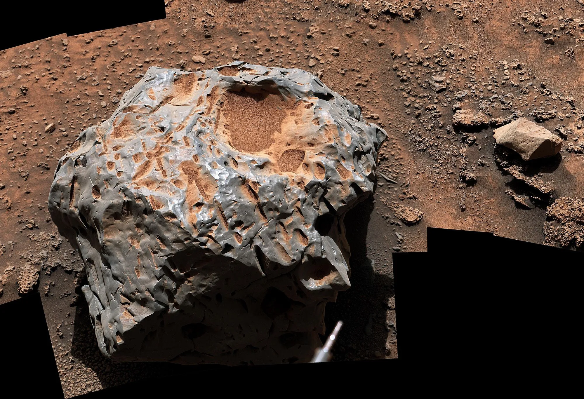 صخرة معدنية غير منتظمة الشكل على سطح المريخ مع تربة حمراء حولها، ملتقطة بواسطة مركبة Curiosity لاستكشاف الكوكب الأحمر.