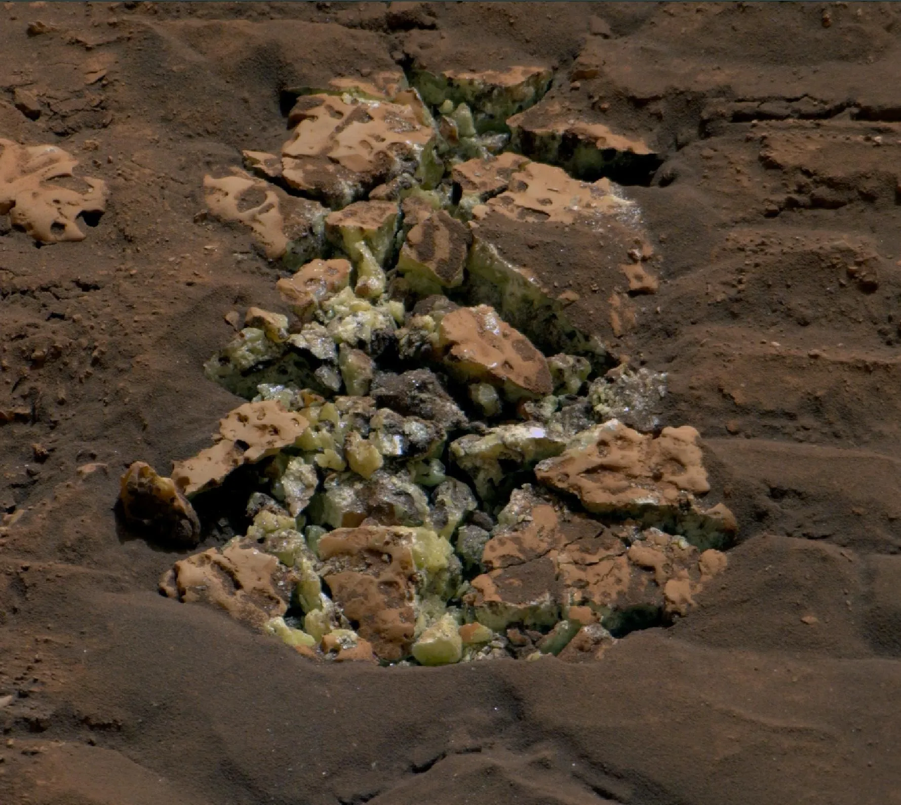 صخور مريخية متكسرة تكشف عن بلورات خضراء داخل حفرة على سطح المريخ التقطتها مركبة Curiosity ضمن دراسة جيولوجية.