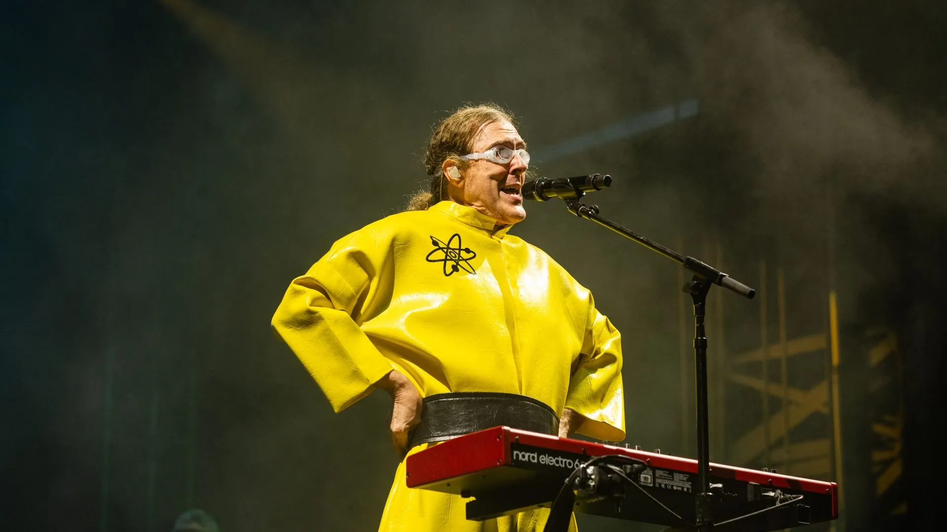 الفنان الكوميدي "Weird Al" Yankovic يرتدي زيًا أصفر مزينًا برمز ذرة أثناء أداء موسيقي على المسرح، احتفالًا بتكريمه بتسمية كويكب باسمه في حزام الكويكبات بين المريخ والمشتري.