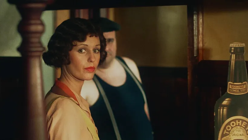 امرأة تعمل خلف حانة في سيدني عام 1925، تعكس مشهدًا من فيلم "Caddie" الذي يسلط الضوء على استقلالية المرأة في الطبقة العاملة.