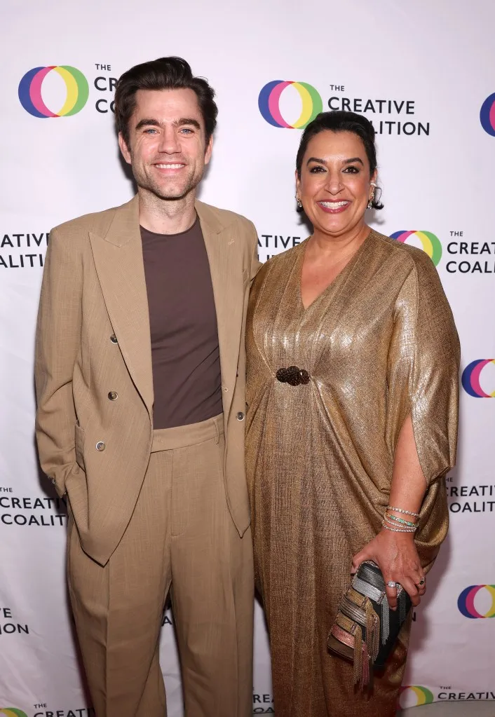 شاب وامرأة يرتديان ملابس أنيقة ويبتسمان أمام خلفية شعار The Creative Coalition في حفل جوائز التلفزيون الإنسانية السنوية.