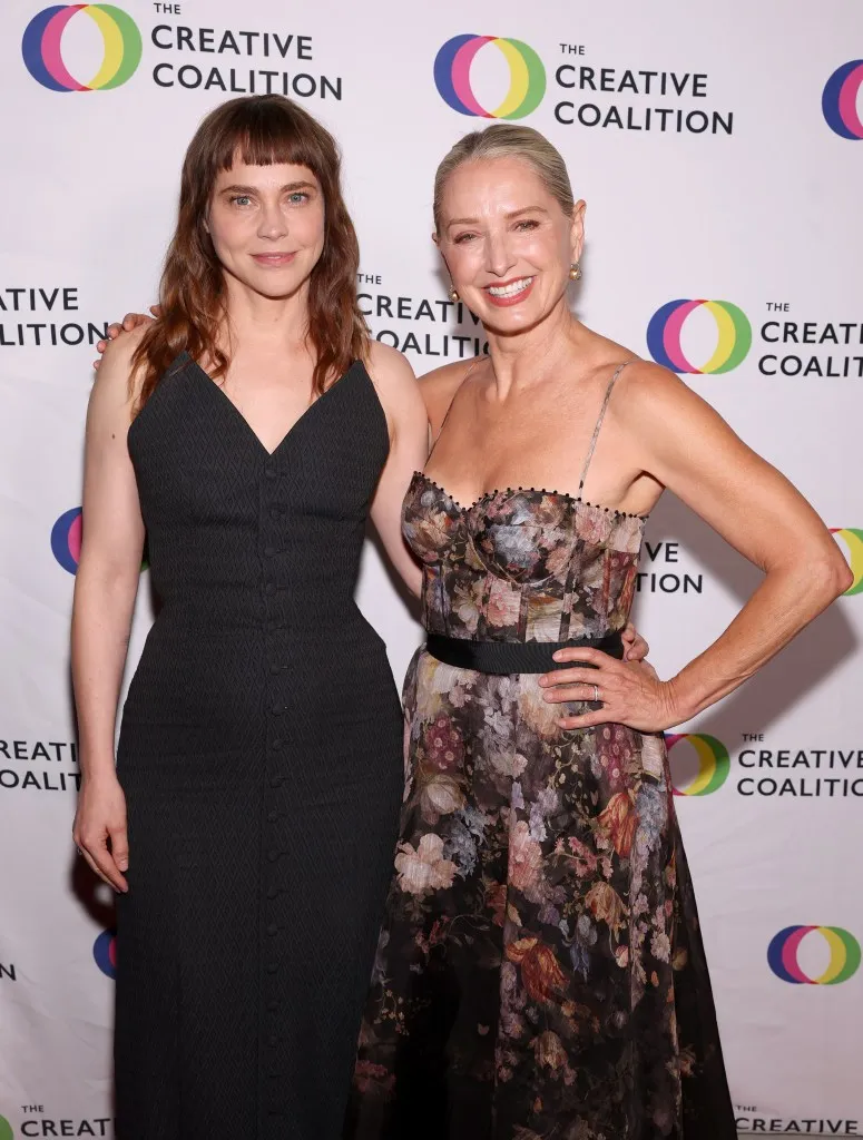 امرأتان مبتسمتان ترتديان فستانين أنيقين تقفان أمام خلفية شعار The Creative Coalition في حفل جوائز التلفزيون الإنسانية السنوي.