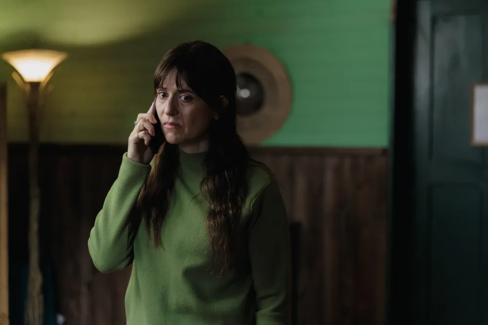 امرأة ترتدي سترة خضراء تتحدث بقلق عبر الهاتف في مشهد من مسلسل Patagonia الإسباني التشيلي عن البحث عن الابن المفقود.
