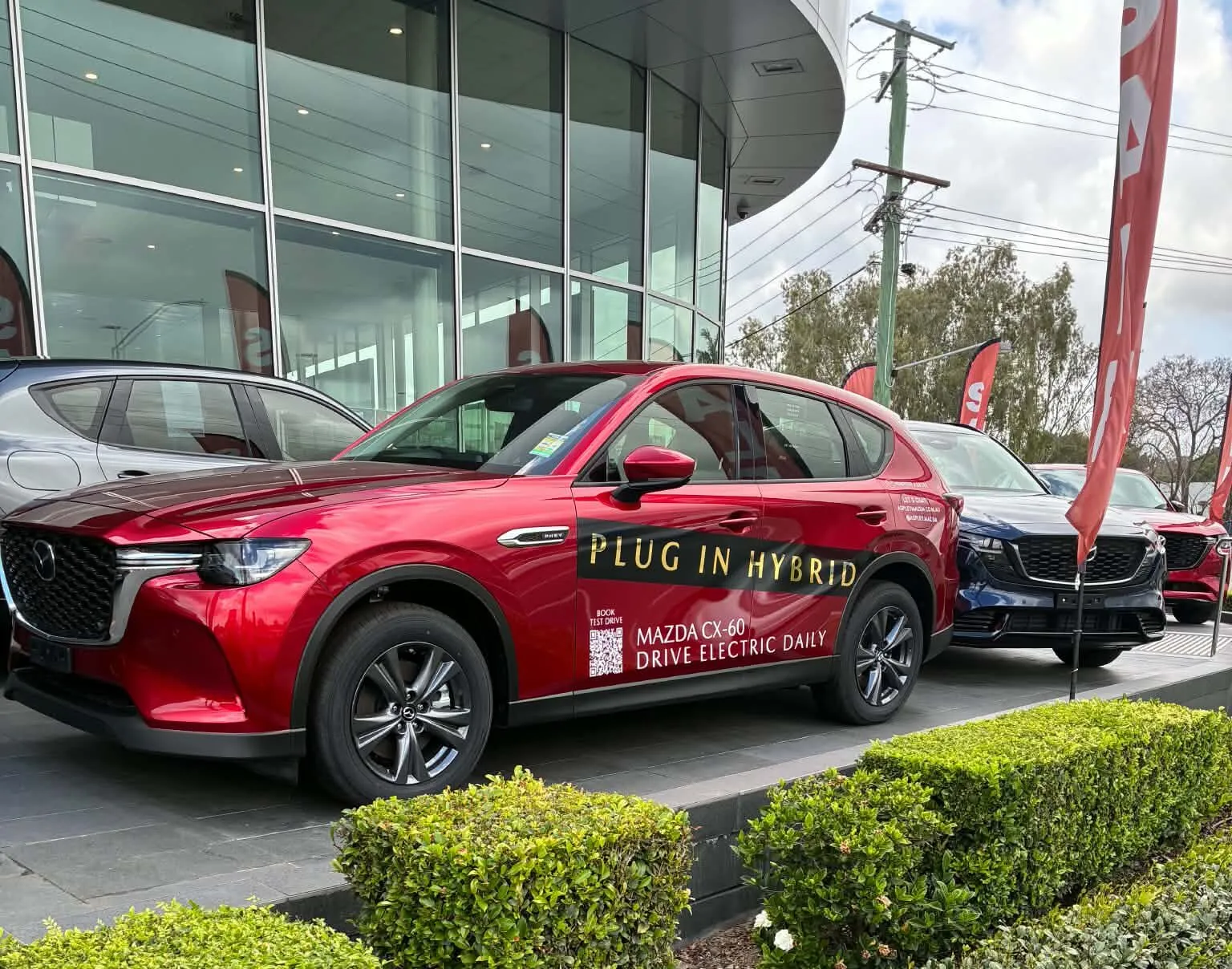 سيارة Mazda CX-60 الهجينة القابلة للشحن باللون الأحمر مع لافتة "PLUG IN HYBRID" معروضة في صالة عرض في بريزبين، أستراليا.