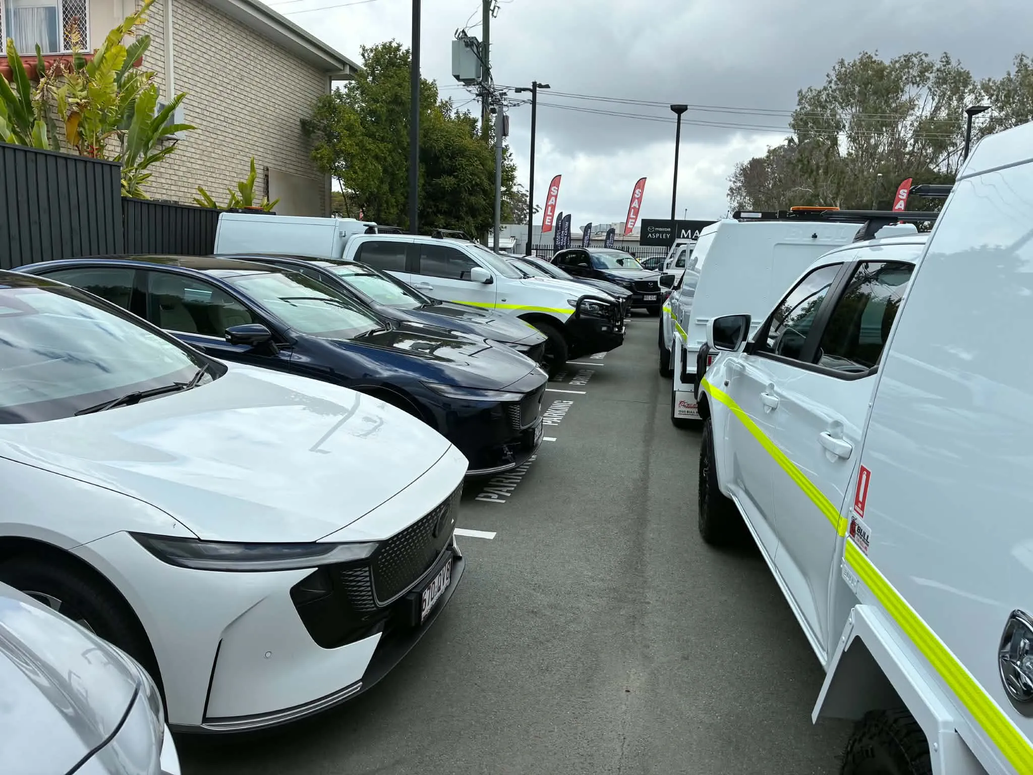 سيارات Mazda 6e الكهربائية والهجينة متوقفة في معرض بريزبين، محجوبة جزئياً بشاحنات BT 50 مما يعيق تجربة القيادة.