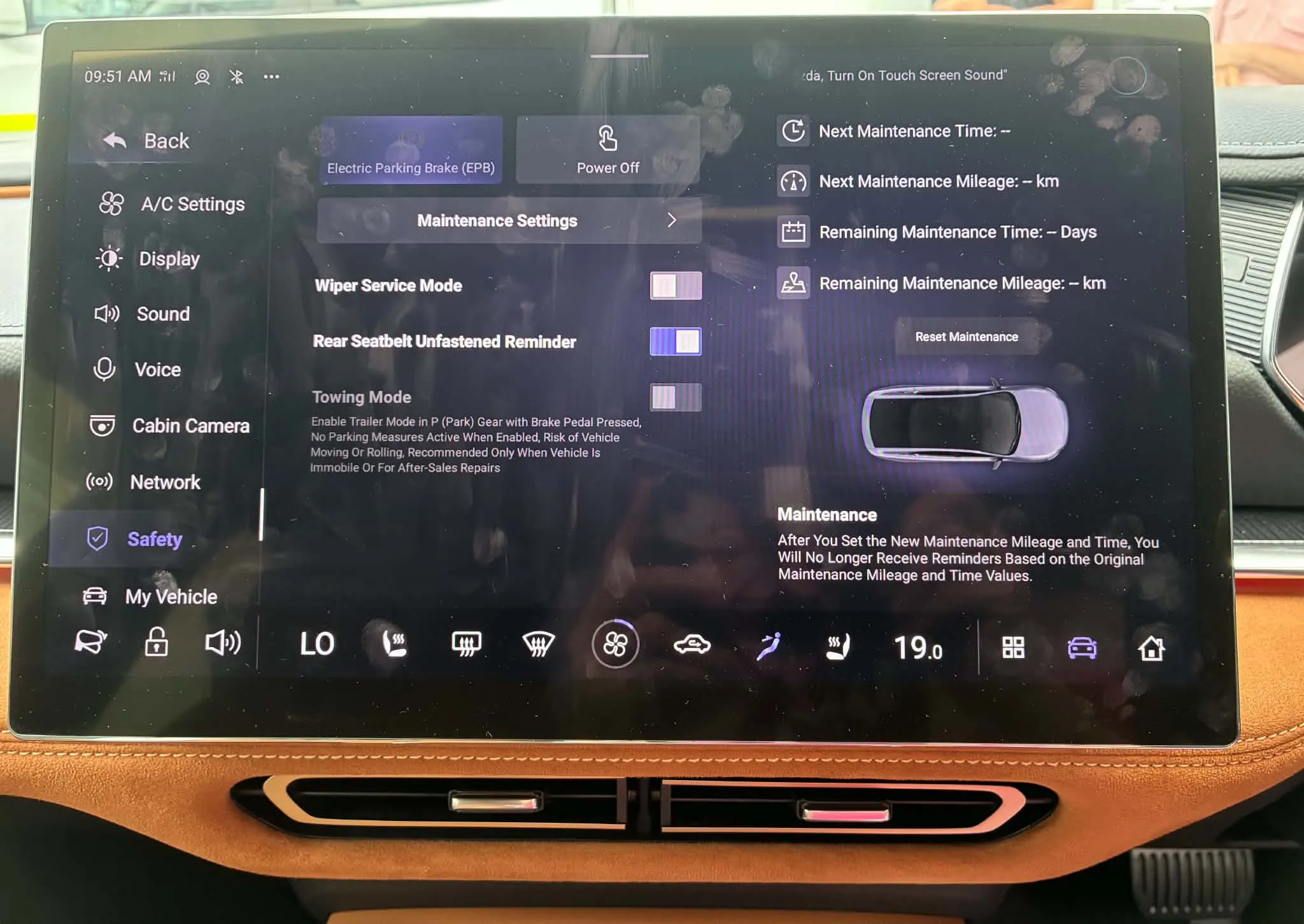 شاشة تحكم داخلية لسيارة Mazda 6e الكهربائية تعرض إعدادات الصيانة والسلامة مع واجهة رقمية حديثة ومقود جلدي بني.