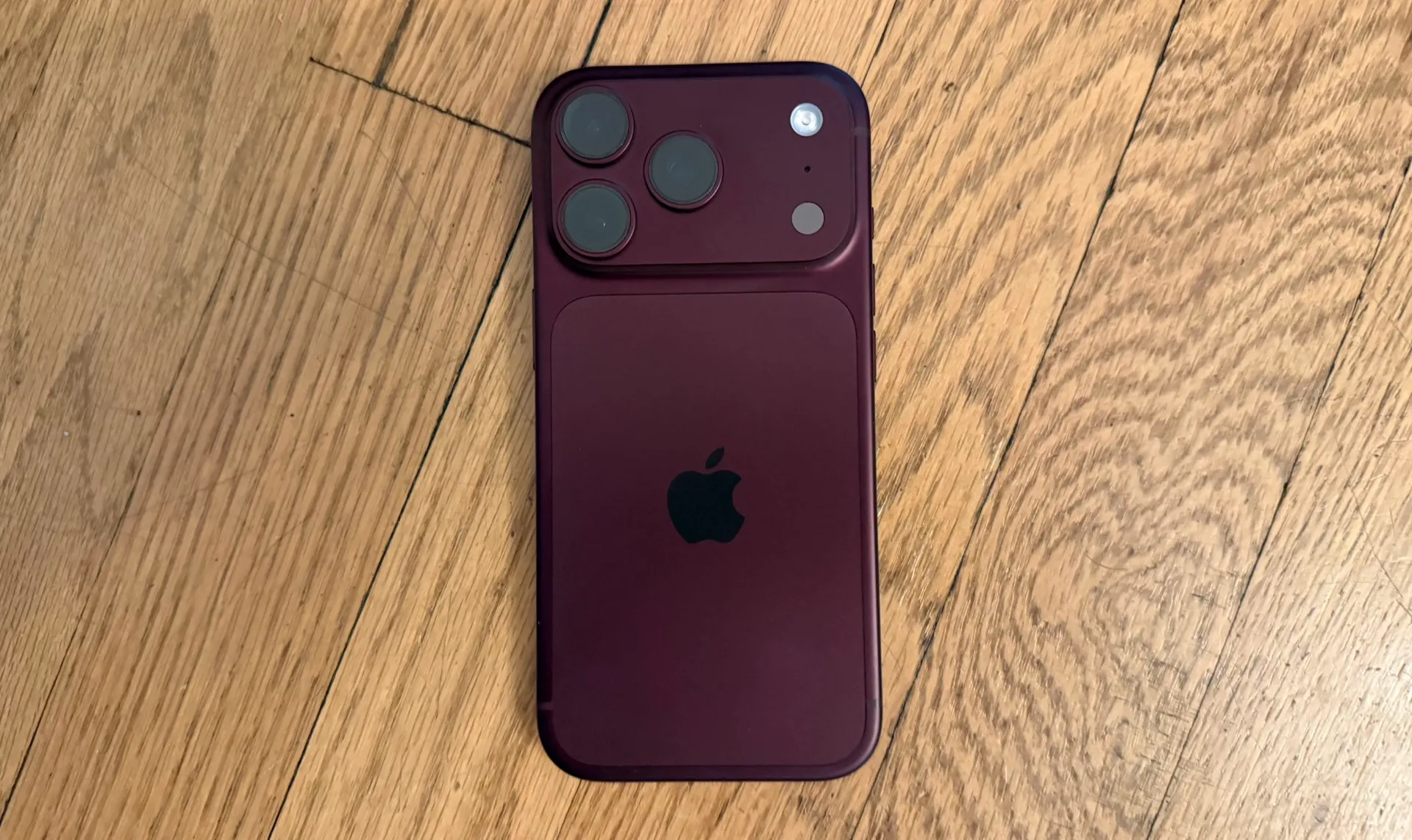 هاتف iPhone 18 Pro باللون العنابي يعرض تصميمًا مشابهًا لـ iPhone 17 Pro مع ثلاث كاميرات خلفية وشعار Apple في مركز الغطاء الخلفي.
