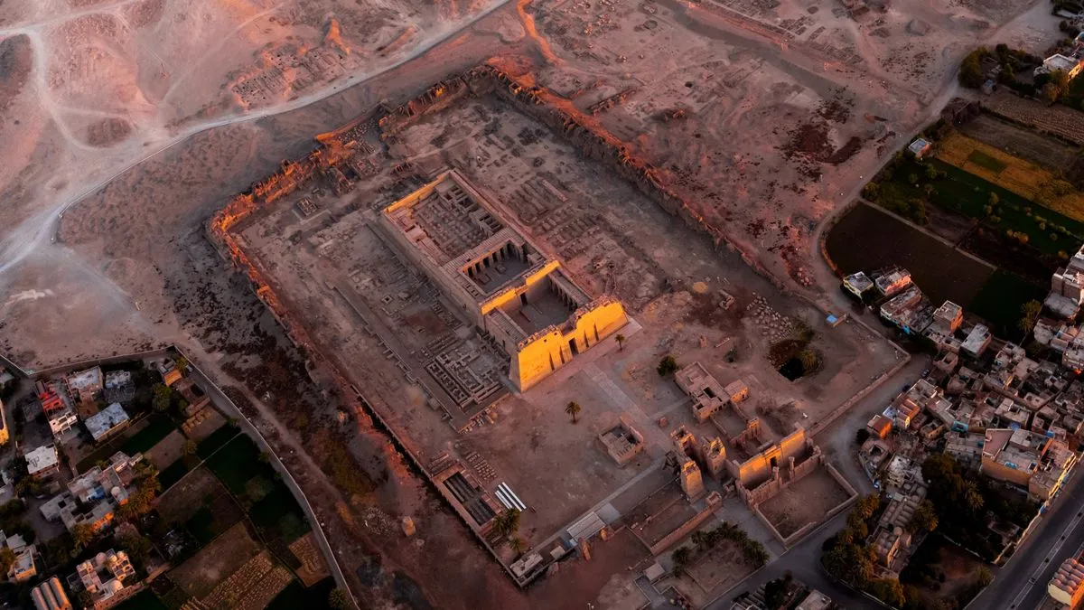 معبد الأقصر من الأعلى عند الغروب، يظهر تفاصيل الأعمدة والآثار المحيطة وسط الصحراء وقرب مساكن المدينة، موقع تاريخي فرعوني بارز.